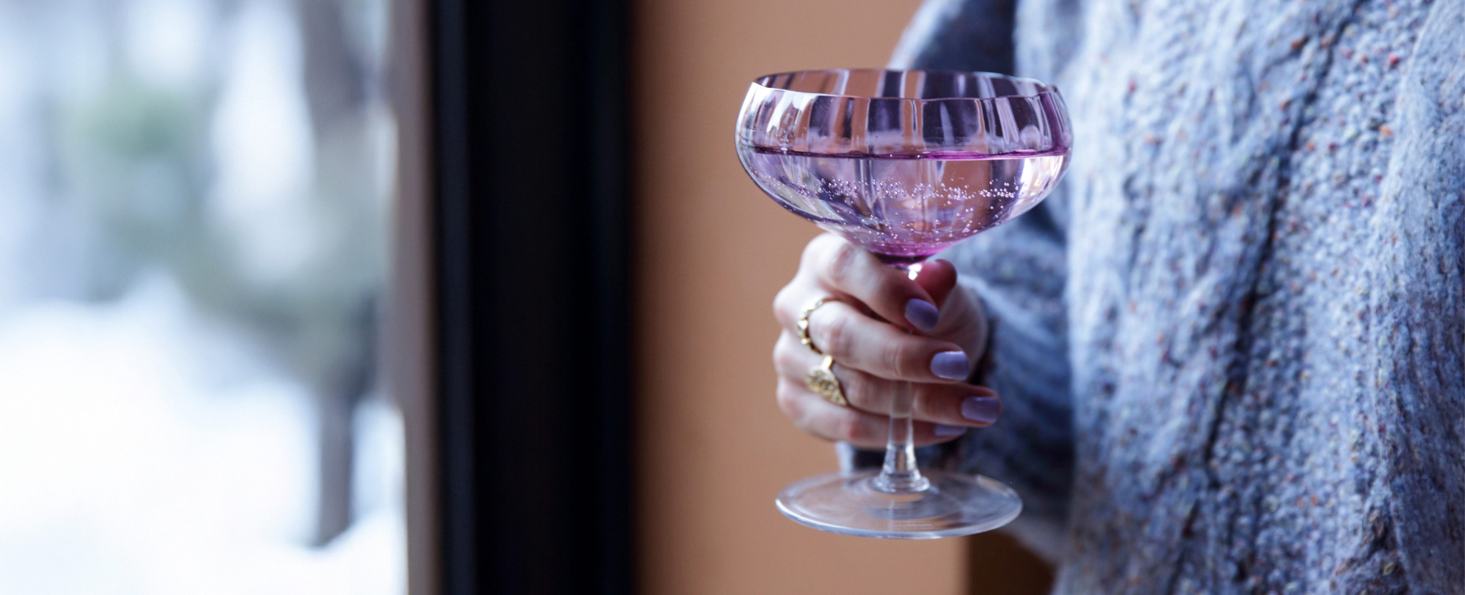Udsnit at kvinde i blå striktrøje, der står med et rosa cocktail glas i hånden.
