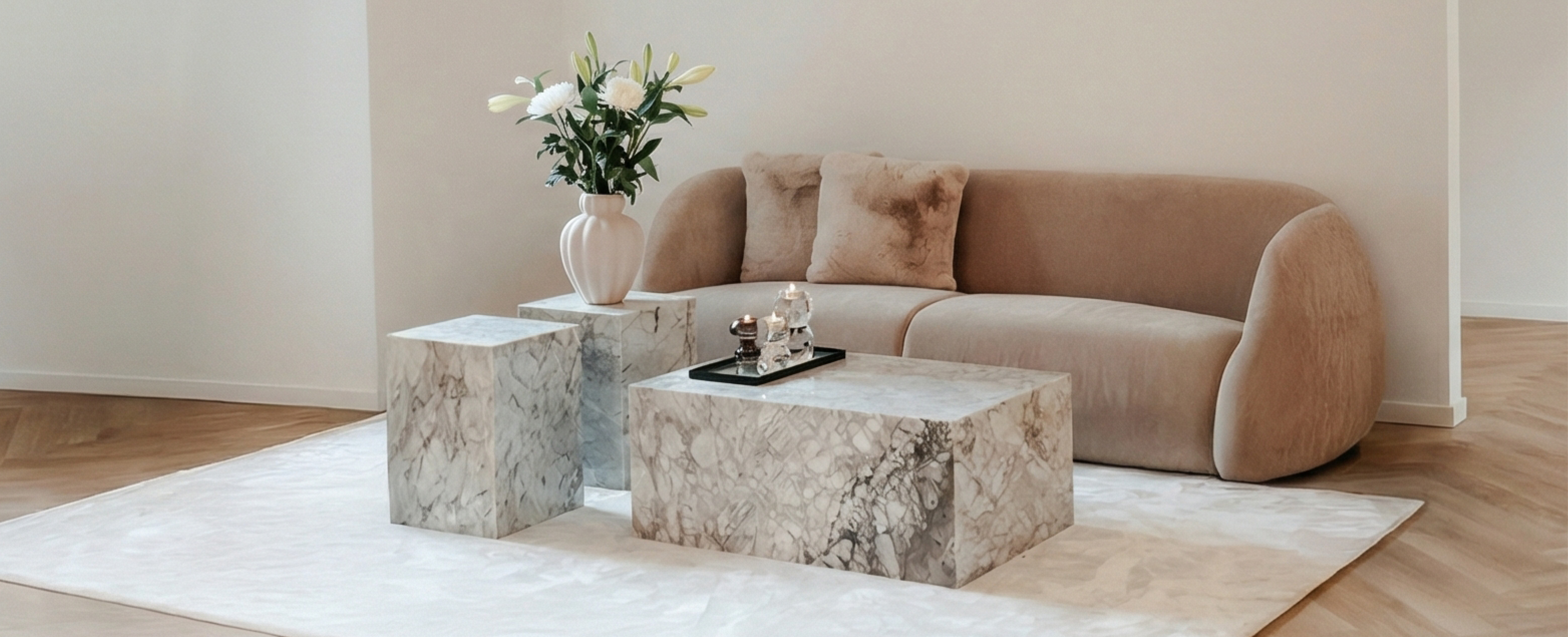 Sofaområde med en brun sofa og beige puder, foran står et gråt marmor sofabord og to marmor sideborde. Under ligger et hvidt gulvtæppe