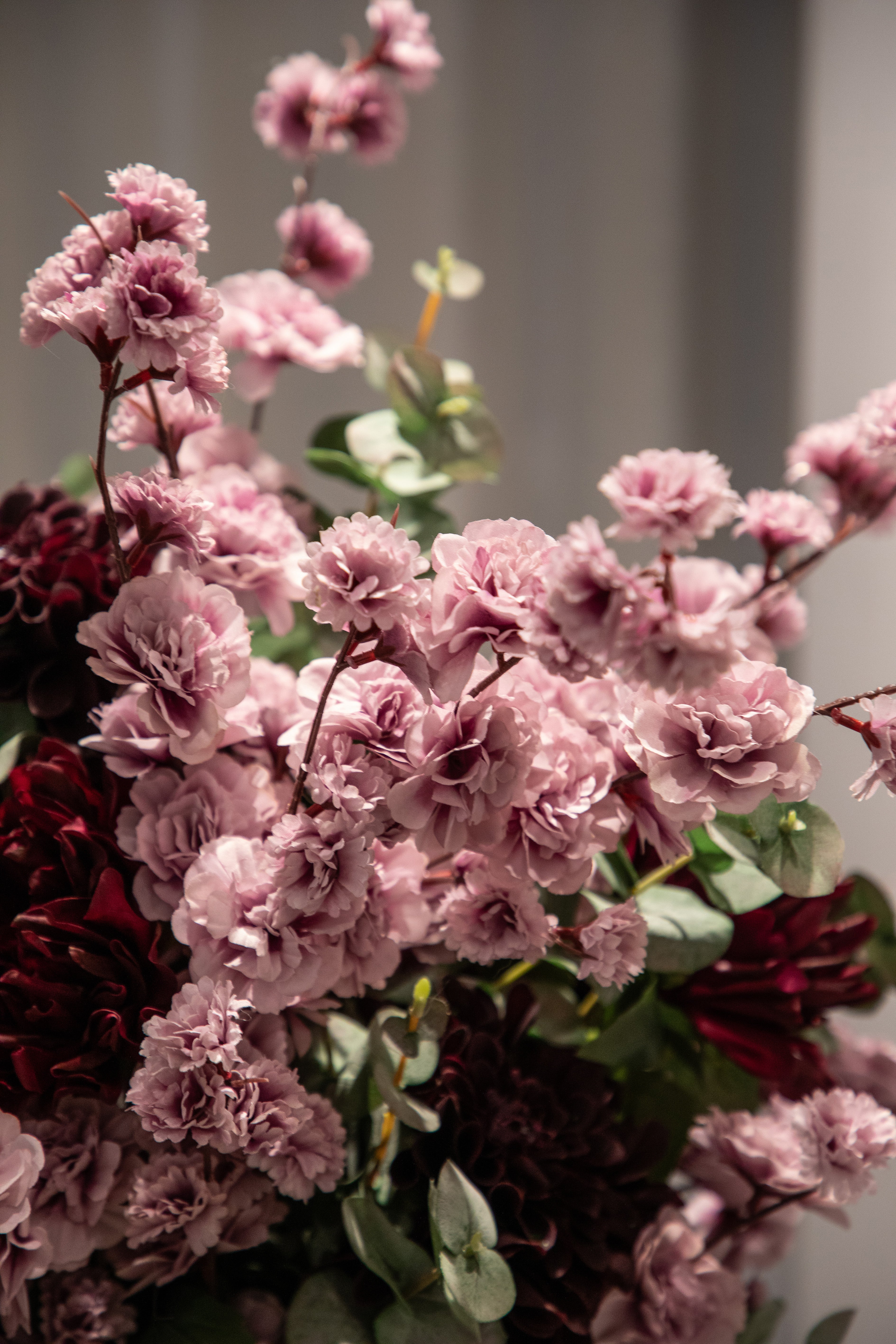 Nærbillede af rose kirsebærstilke, der er del af en større kunstig buket i rose, grønne og bordeaux nuancer.