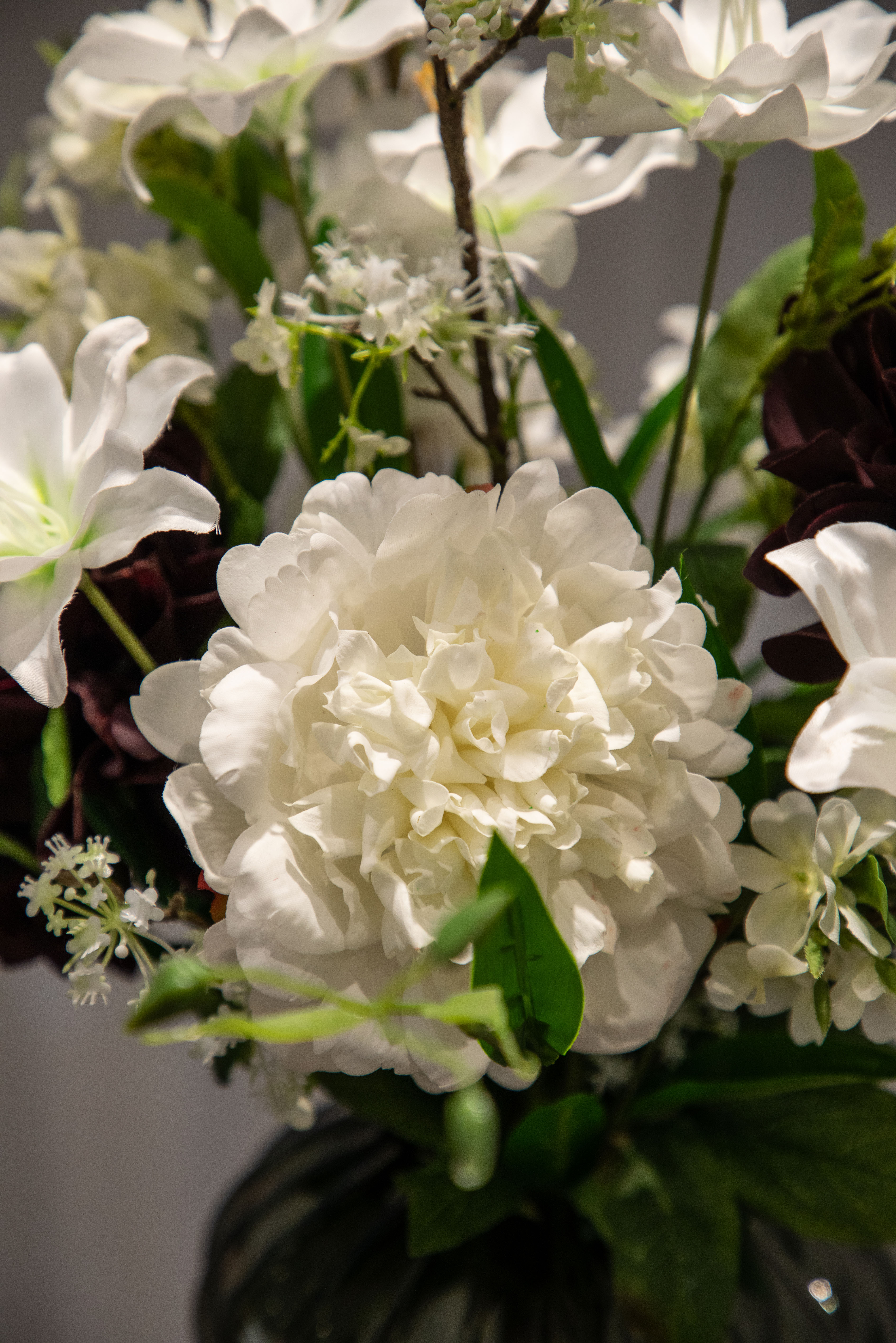 Nærbillede af hvid pæon stilk, der er del af en større kunstig buket i hvide, grønne og bordeaux nuancer.