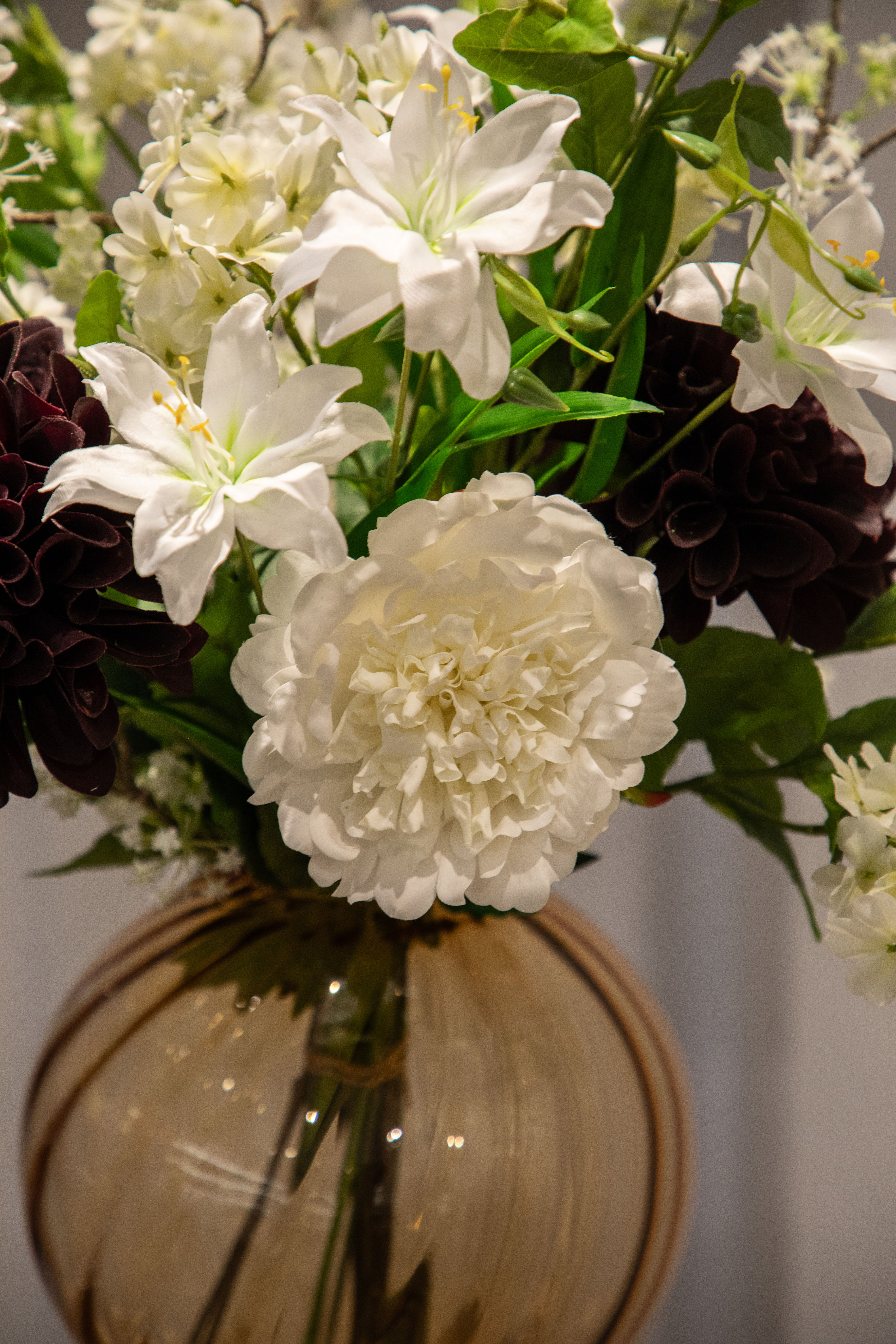 Nærbillede af kunstig buket i hvide, grønne og bordeaux nuancer, der står i en orange glas vase.