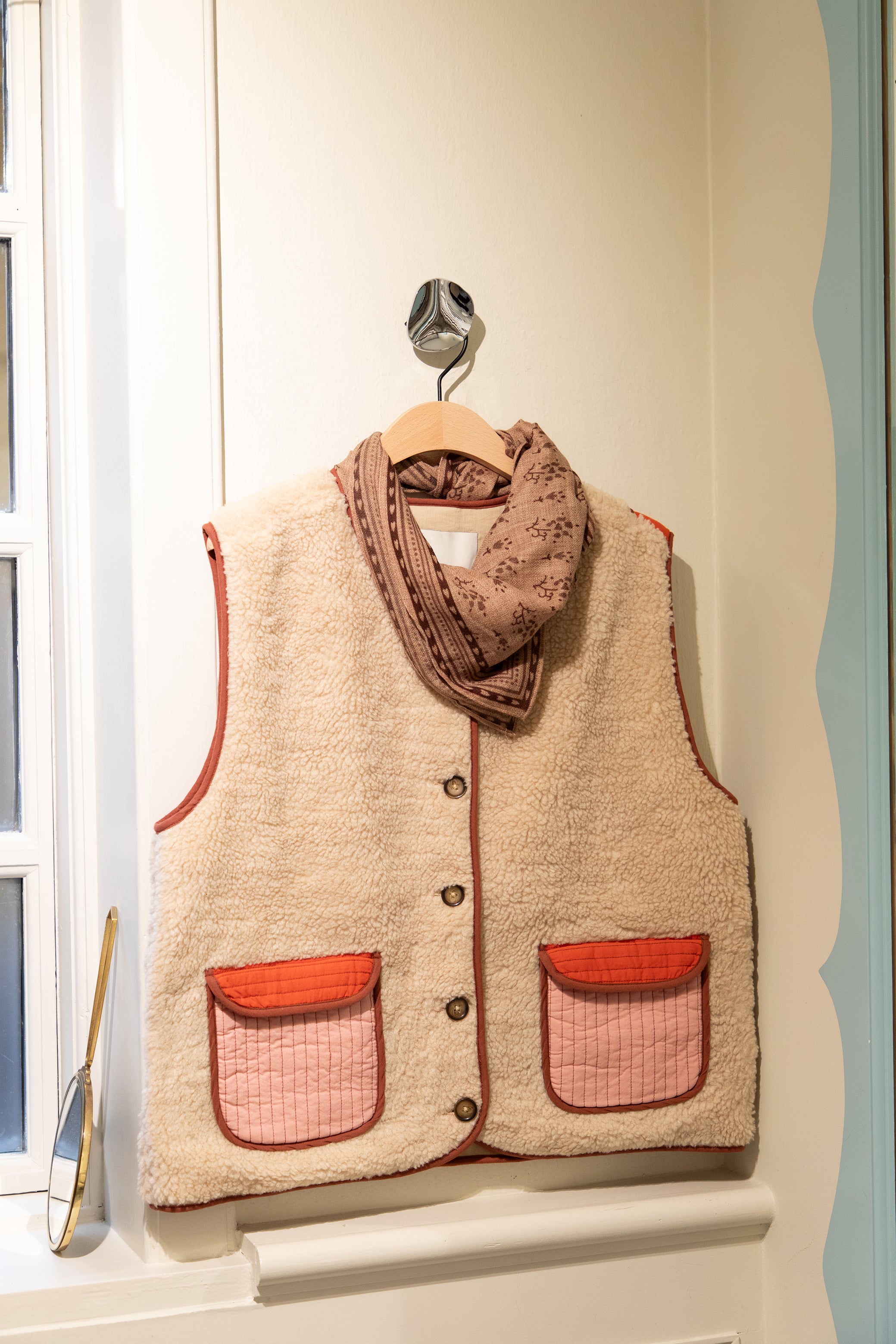 Amalia knagen i den lille runde version i chrome med en bøjle og tøj hængende fra.