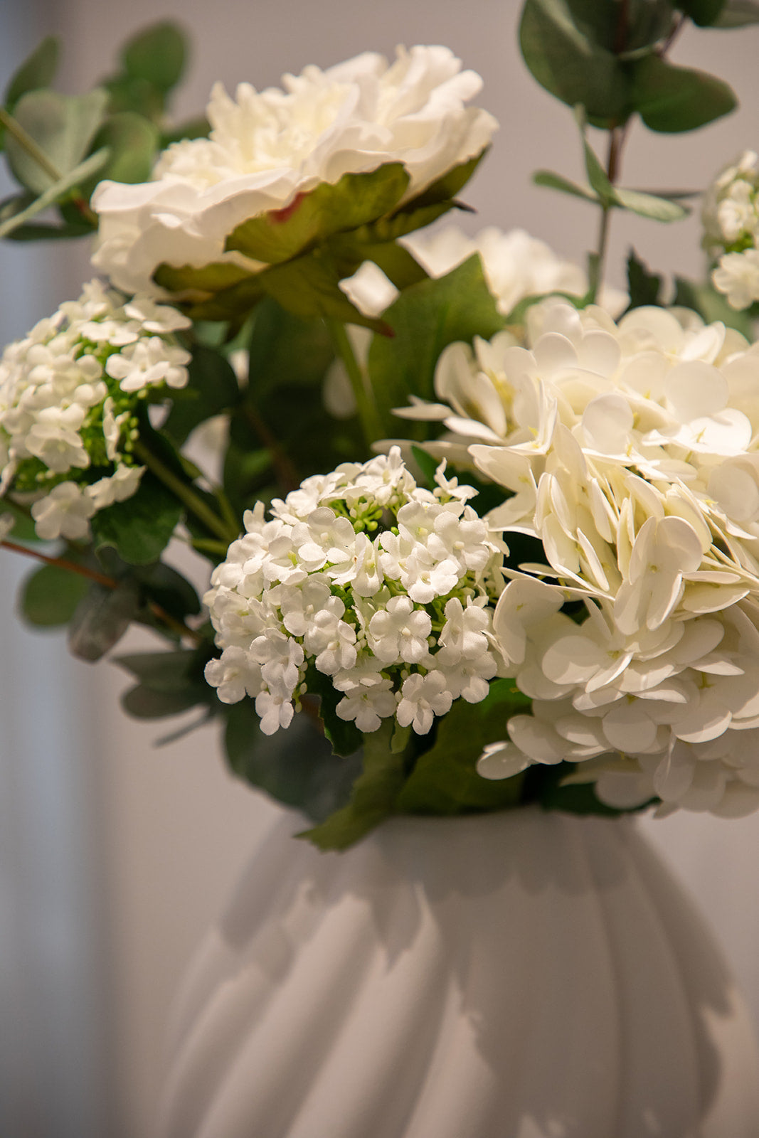 Nærbillede af kunstig buket i grønne og hvide nuancer, placeret i en hvid keramik vase.