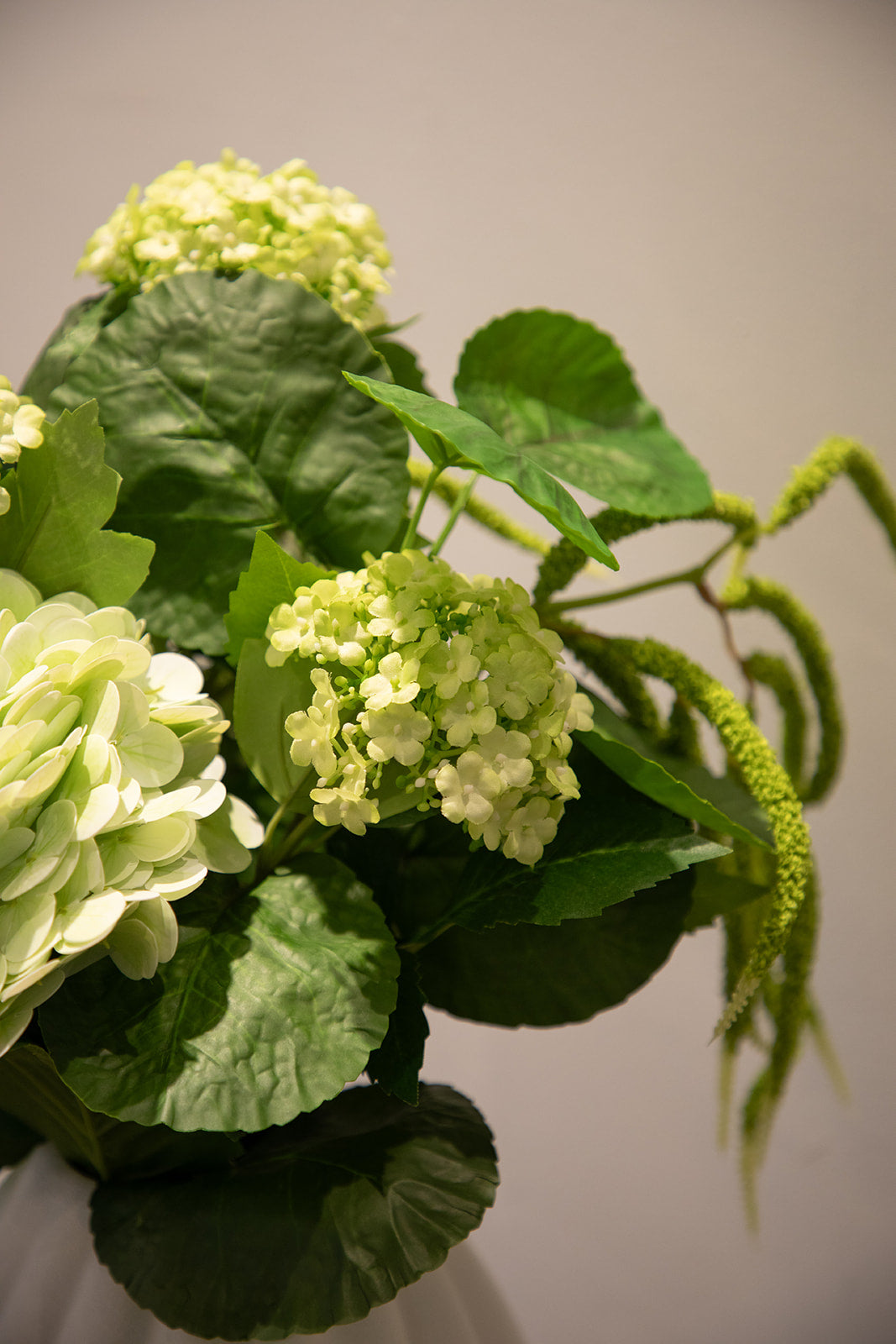 Nærbillede af kunstig buket i grønne nuancer, placeret i en hvid keramik vase.