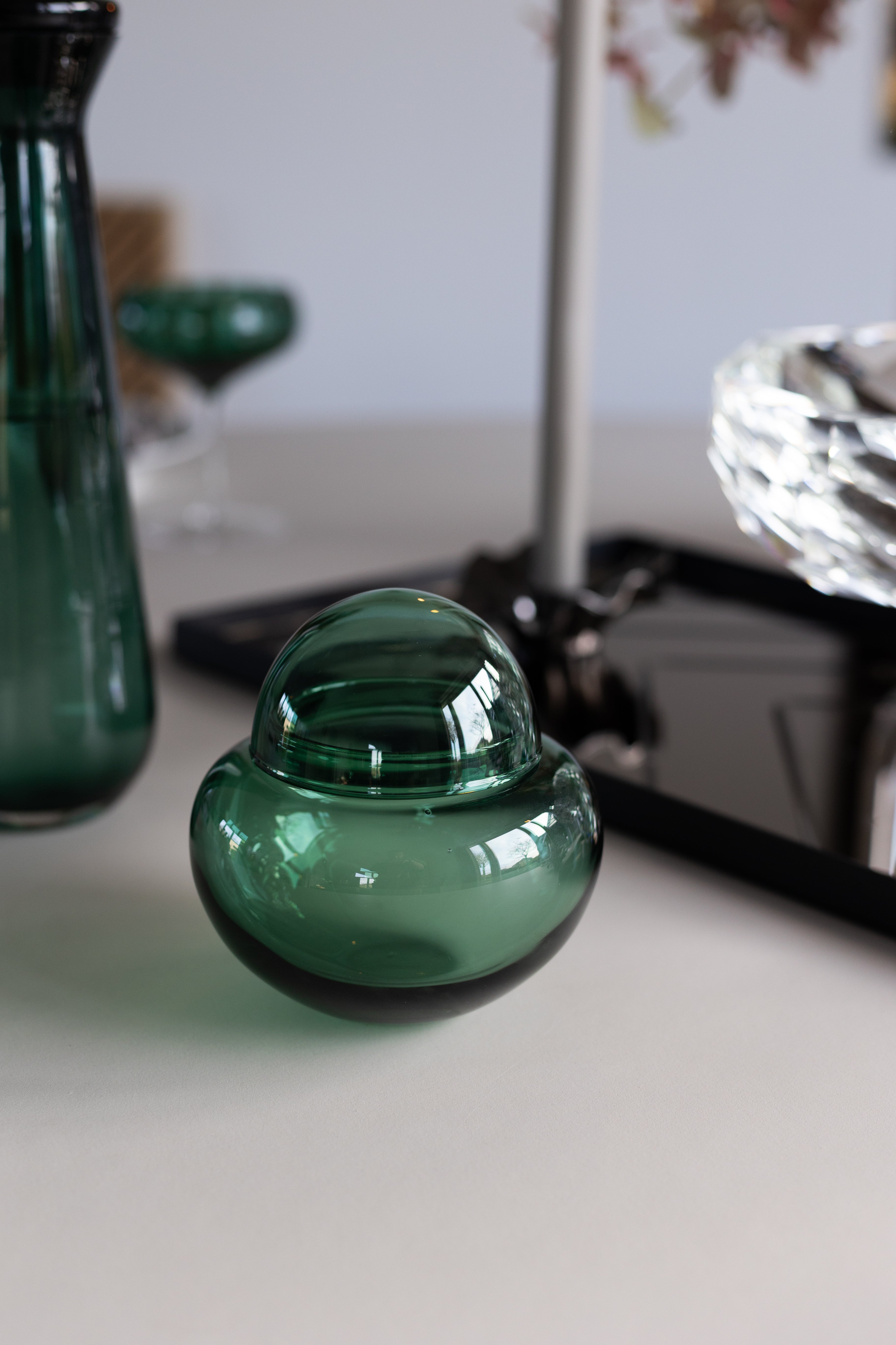 Mundblæst bonbonierre i grønt glas, stylet på et spisebord med andre mundblæste designs i samme serie.