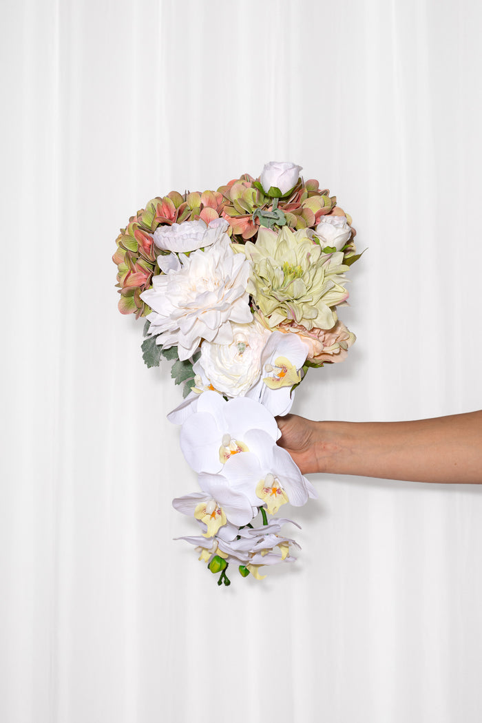 En moderne og chic brudebuket skabt af en orkide, hortensia, dahlia og ranunkel. Farverne er lyse; hvide, lysegrøn, rosa og peach.