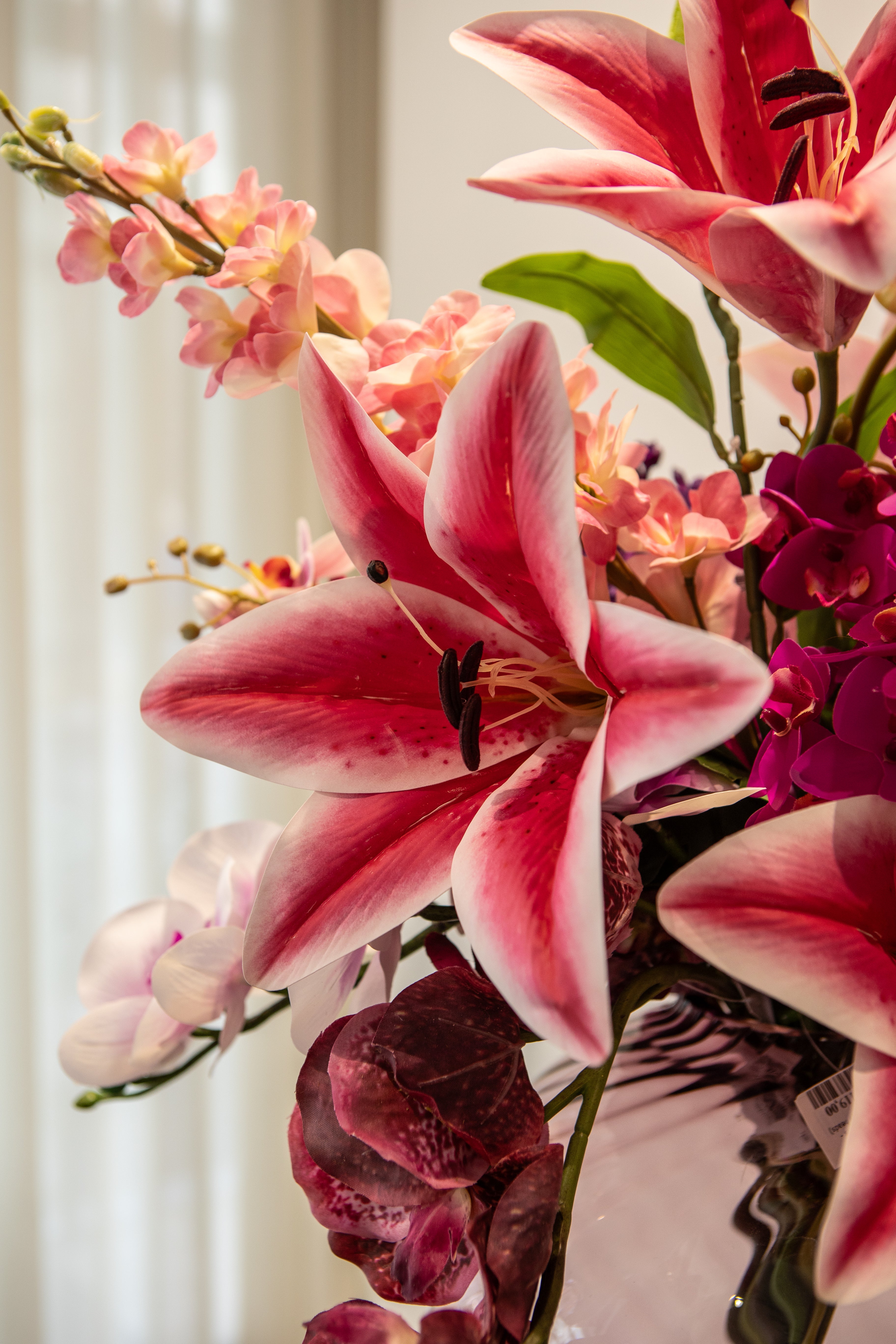 Nære billede af en stor lyserød lilje i en plum farvet buket og glasvase.