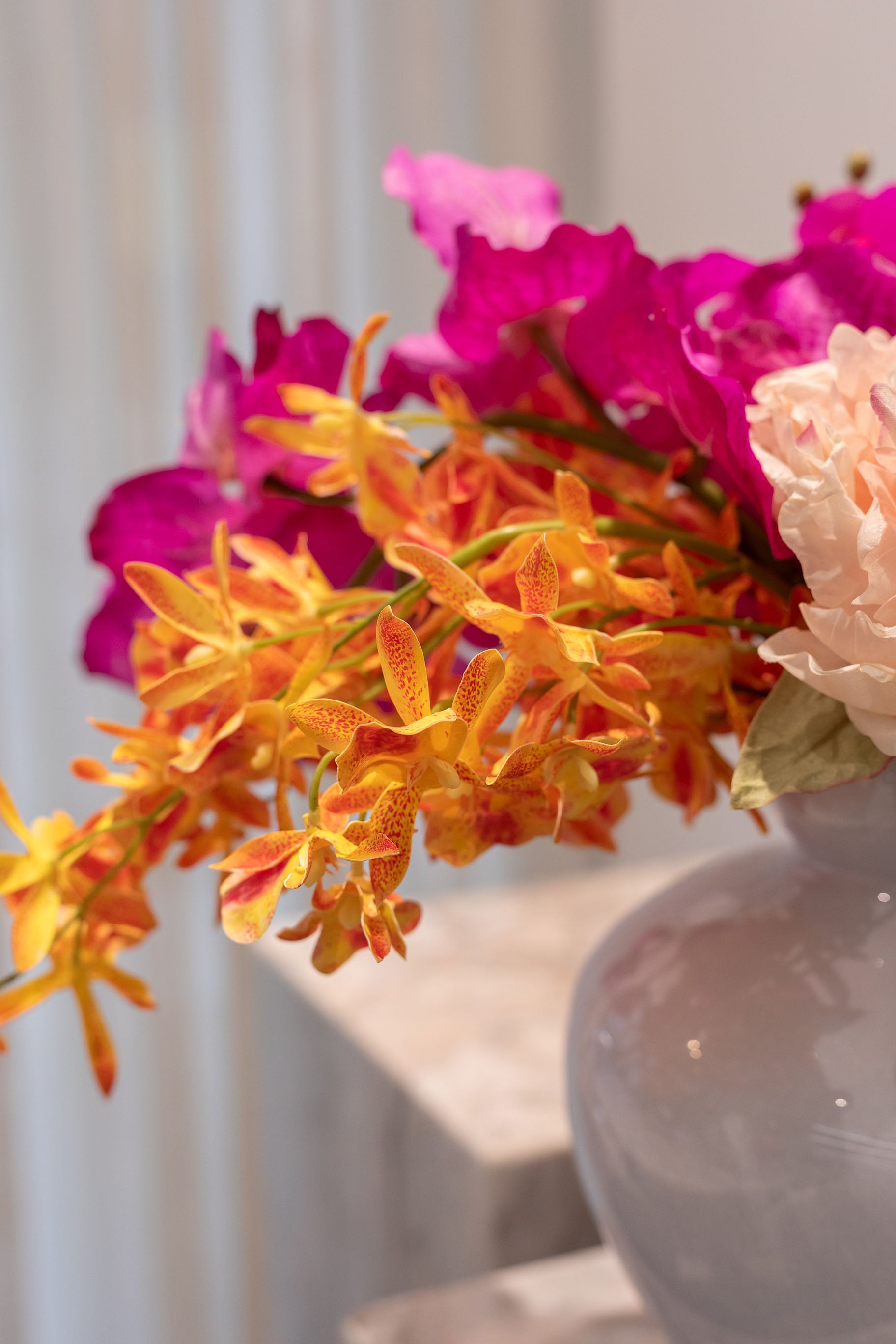 Nærbillede af orange orkidé. En del af en buket af kunstige blomster i lilla, rosa, orange og og grønne nuancer. Placeret i en blå glasvase.