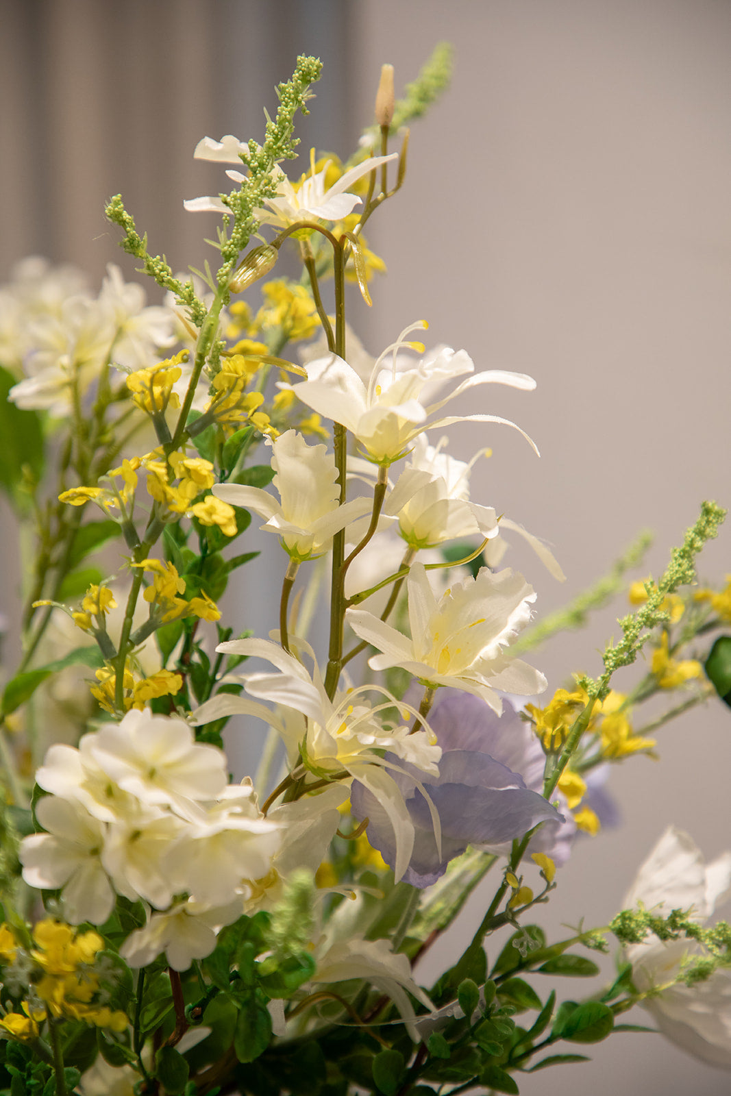 Nærbillede af buket af kunstige blomster i hvide, lilla, gule og grønne nuancer.