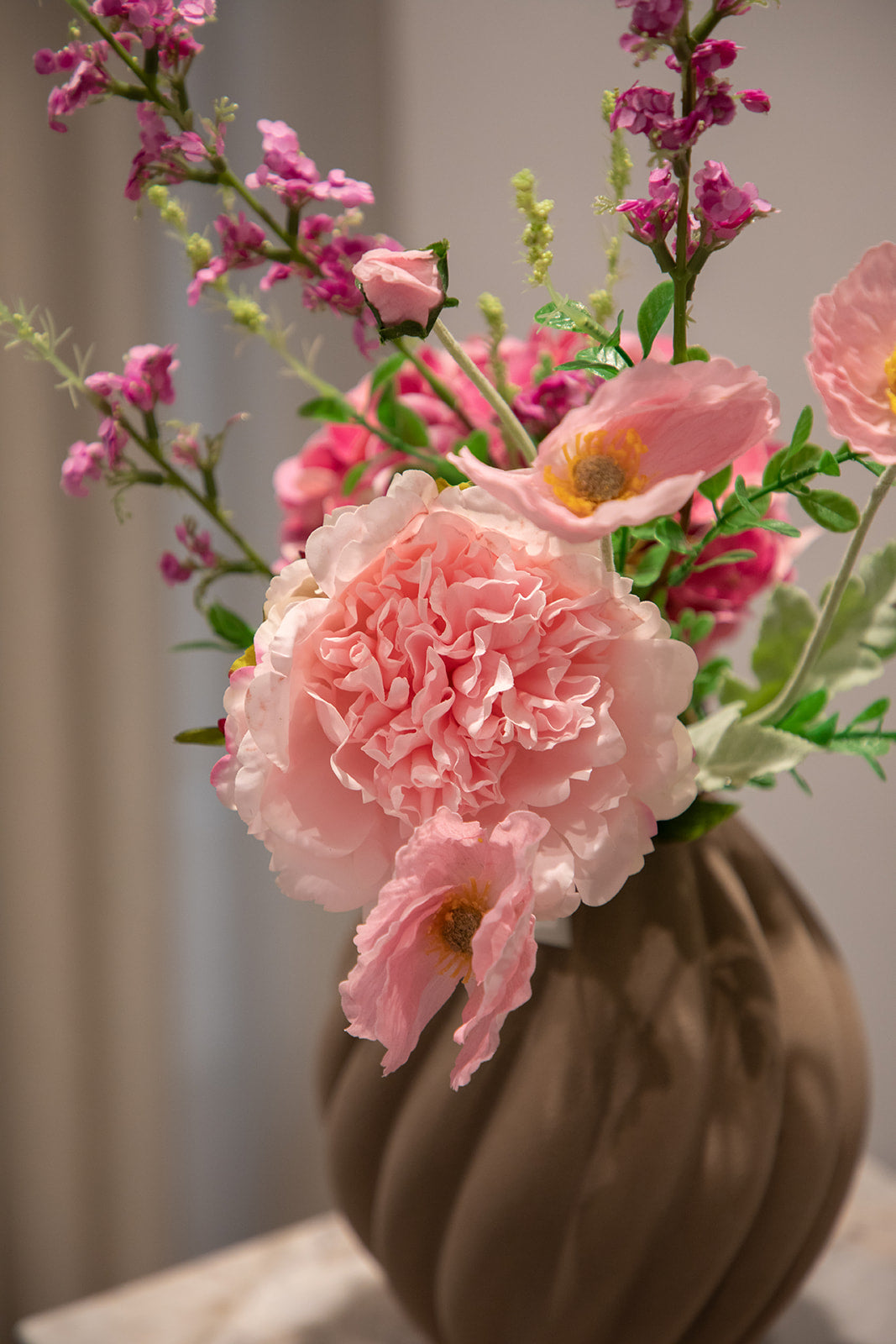 Nærbillede af buket af kunstige blomster i lyserøde nuancer. Placeret i en brun keramikvase.
