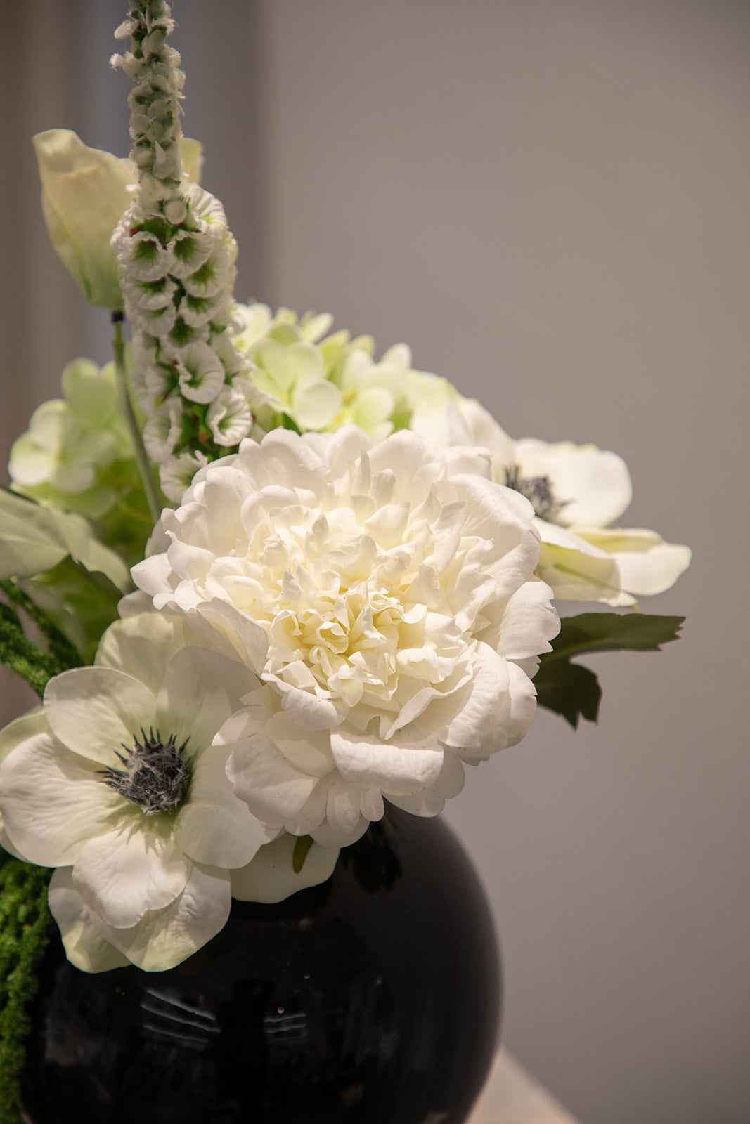 Nærbillede af buket af kunstige blomster i grønne og hvide nuancer, placeret i en blå glasvase.