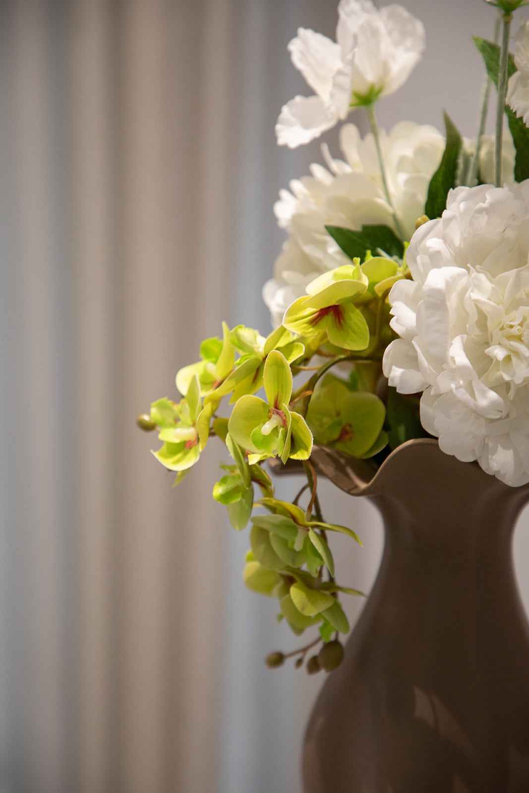 Nærbillede af buket af kunstige blomster i grønne, hvide og rosa nuancer. Placeret i en brun keramikvase.