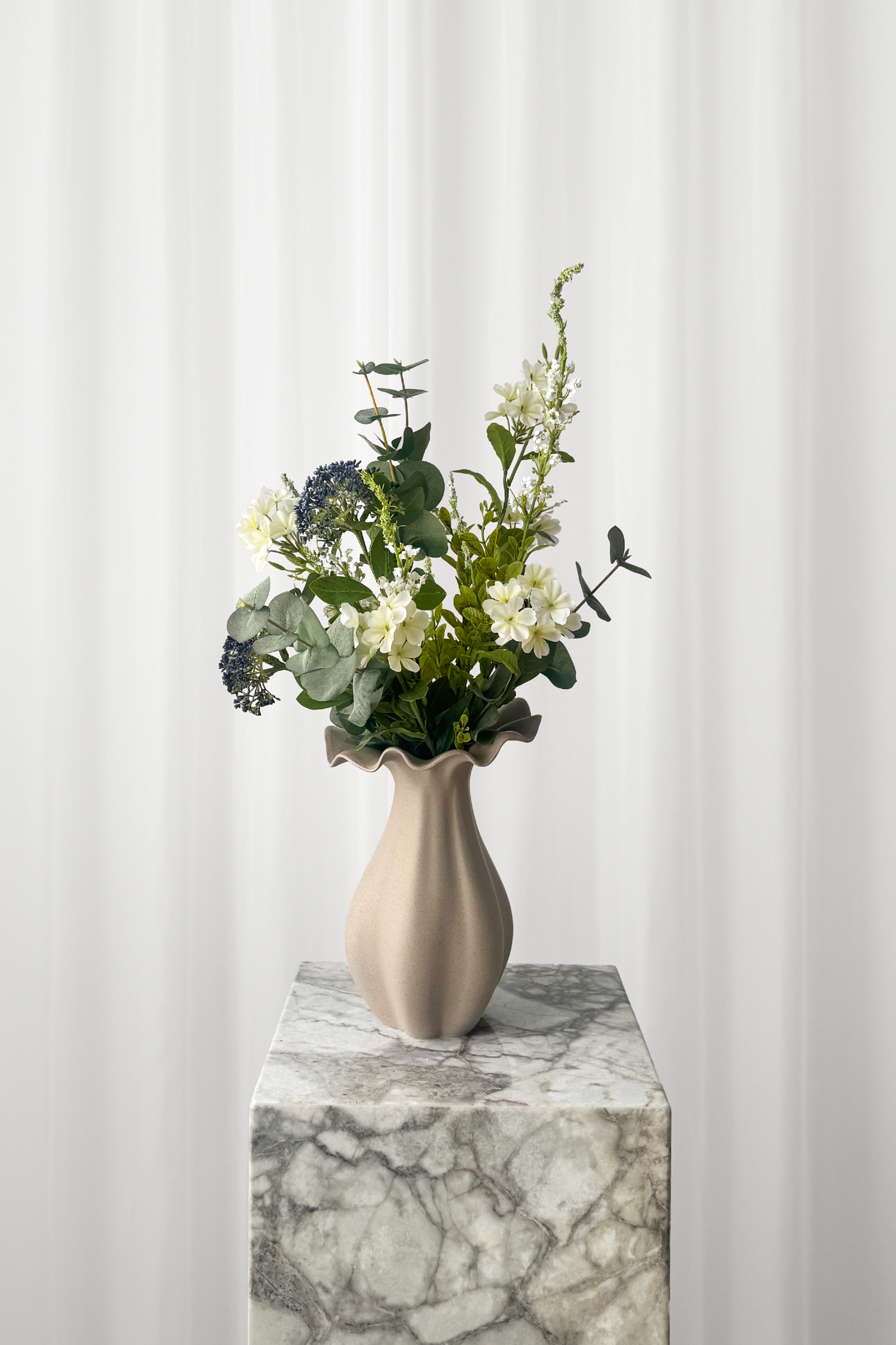 Keramikvase med en luftig buket i grønne og blå farver. Naturtro blomster.