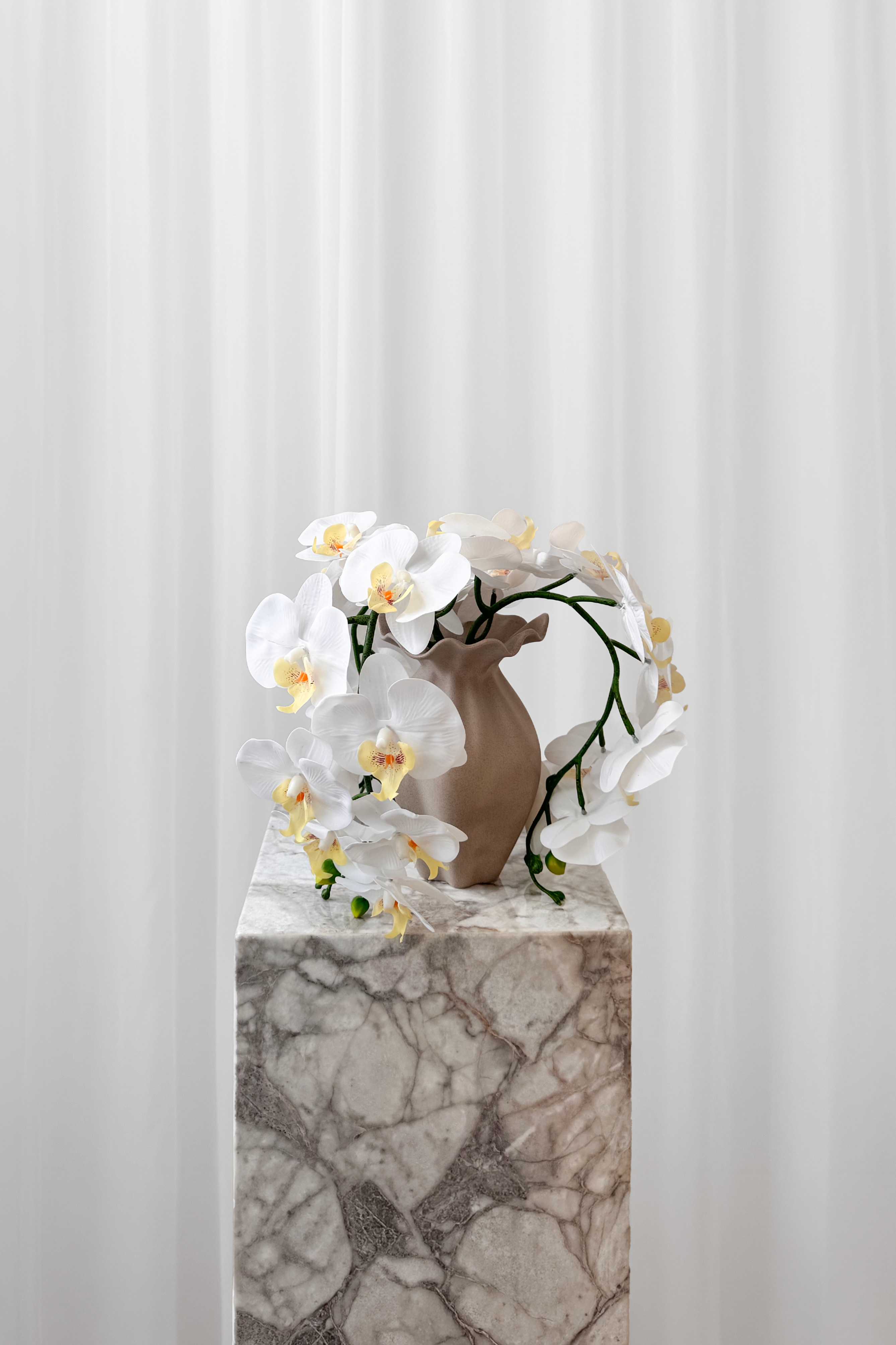 Buket af hvide orkideer stylet i en keramikvase.