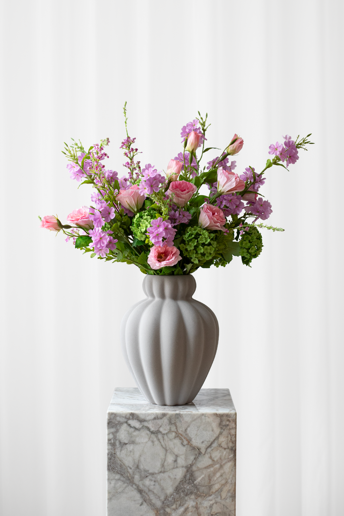 Vild buket af kunstige blomster i lyserøde, lilla og grønne farver, stylet i en Penelope keramikvase fra Specktrum.
