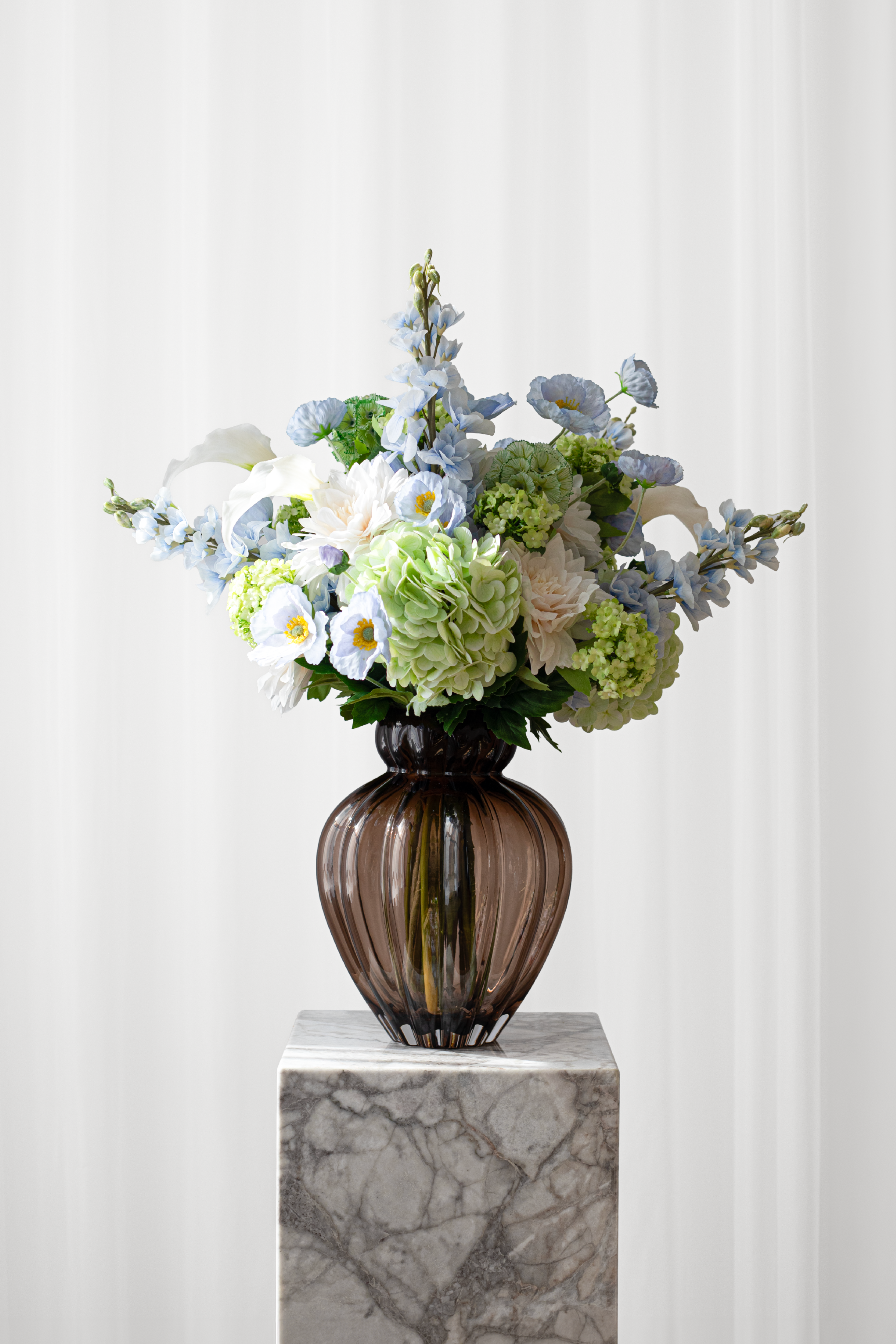kunstig blå buket fra specktrum i blå, hvide og grønne farver. Buketten består af lysegrønne hortensia, hvide calla liljer, hvide dahlia og lyseblå valmuer.