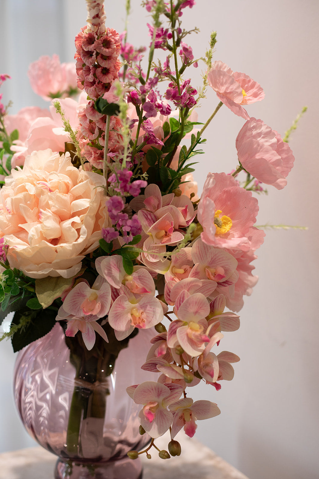 Nærbillede af kunstig buket i lyserøde og creme nuancer, der er placeret i en lyserød glas vase.