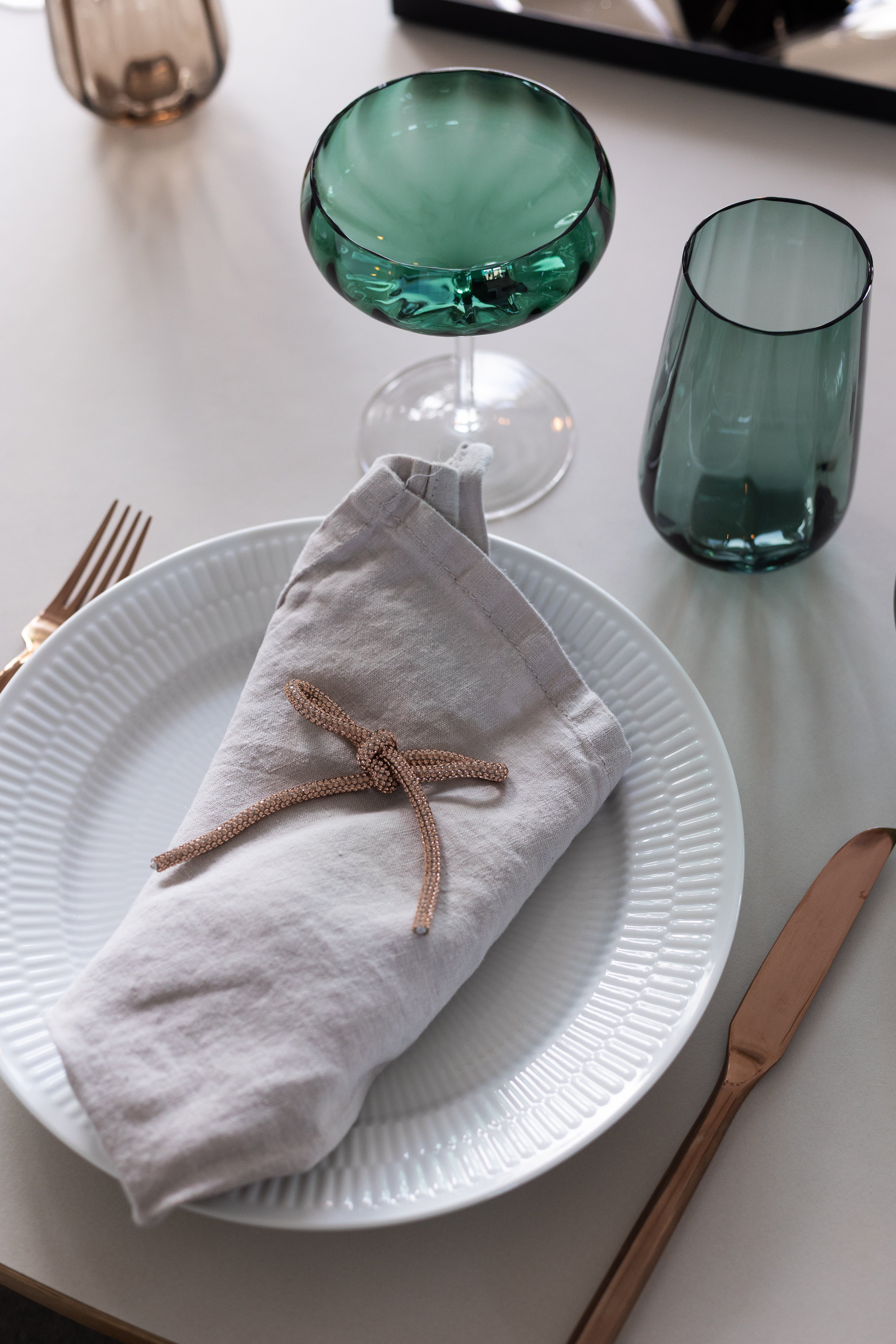 Glimmersløjfe fra Specktrum stylet som en del af borddækningen ovenpå en serviet. Borddækningen inkluderer også cocktailglas og drikkeglas fra Meadow serien.