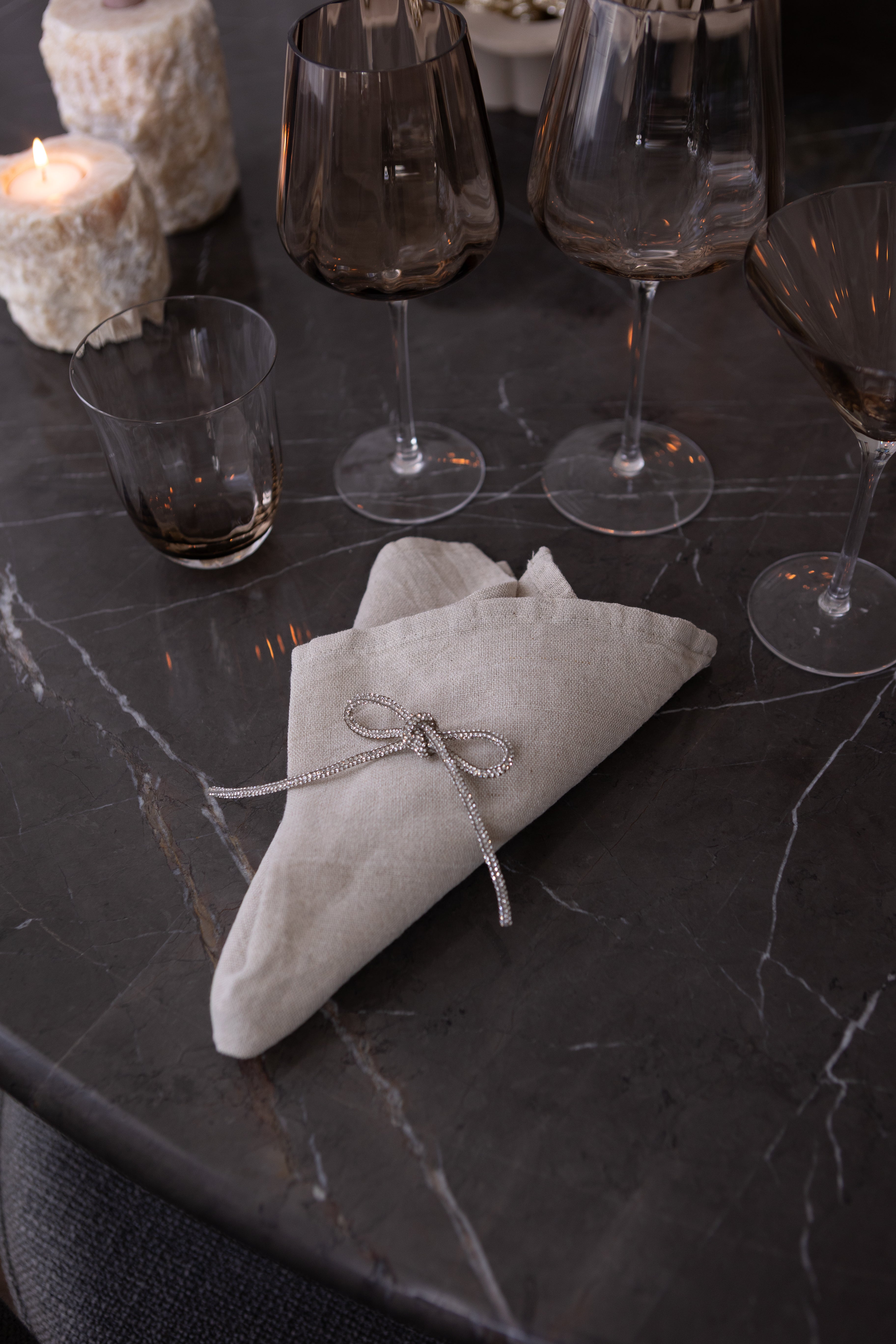 Billede af en glitrende sløjfe, der ligger på en serviet. Der er dækket op på et marmorspisebord med glas i topaz