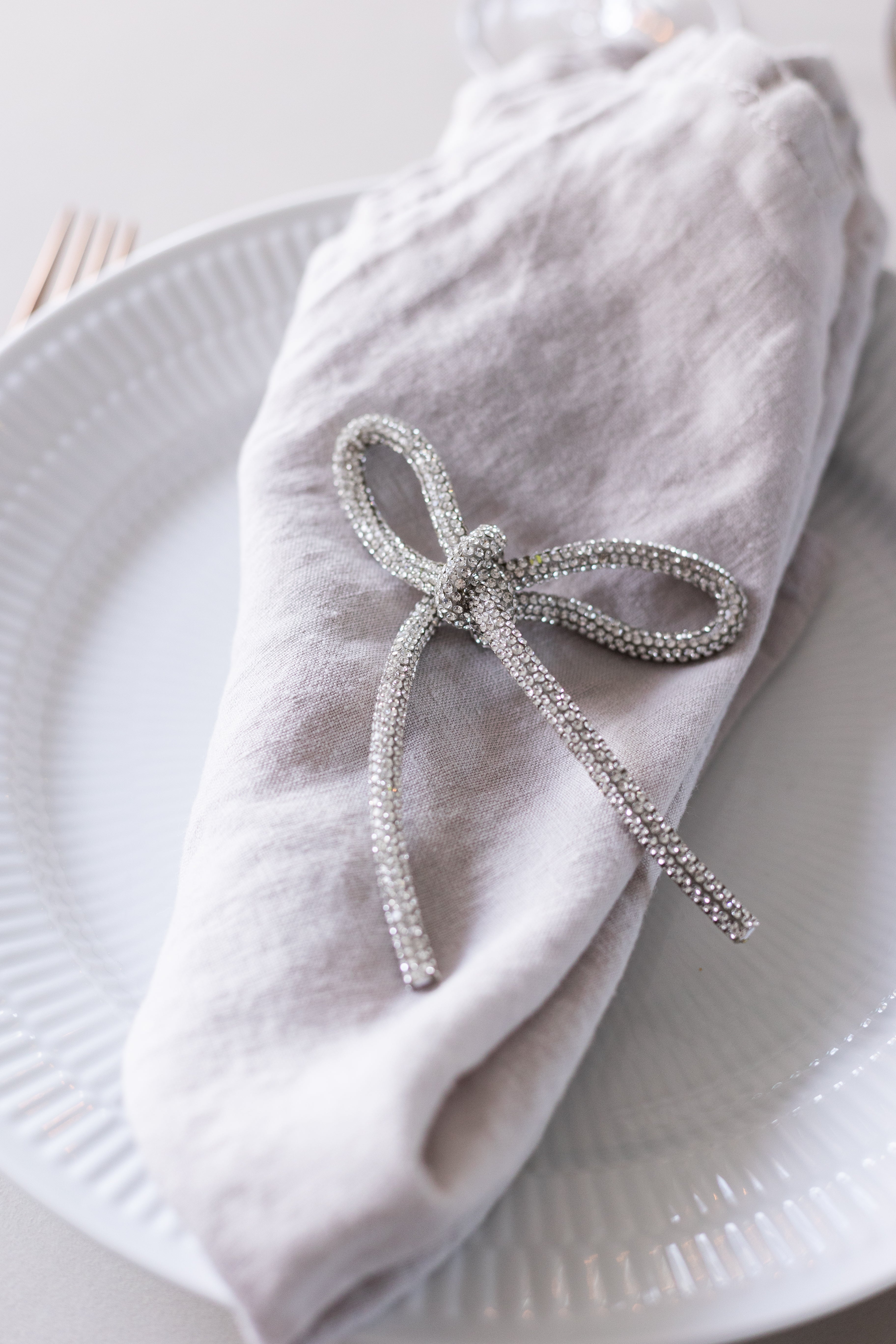 Glittersløjfe i sølv fra Specktrum, der ligger ovenpå servietten som en del af en smuk borddækning.