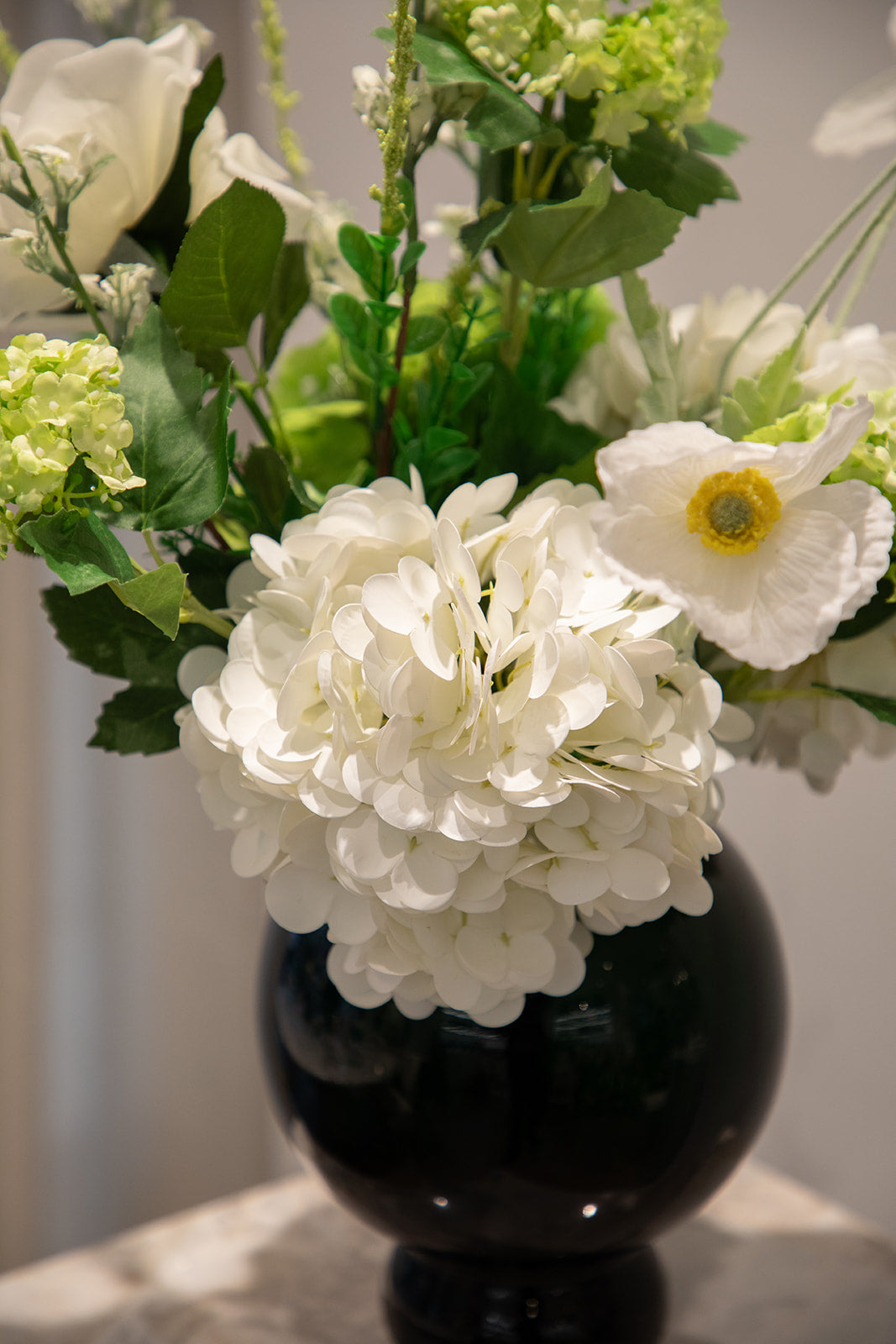 Nærbillede af buket af kunstige blomster i hvide og grønne nuancer. Placeret i en lille blå glasvase.