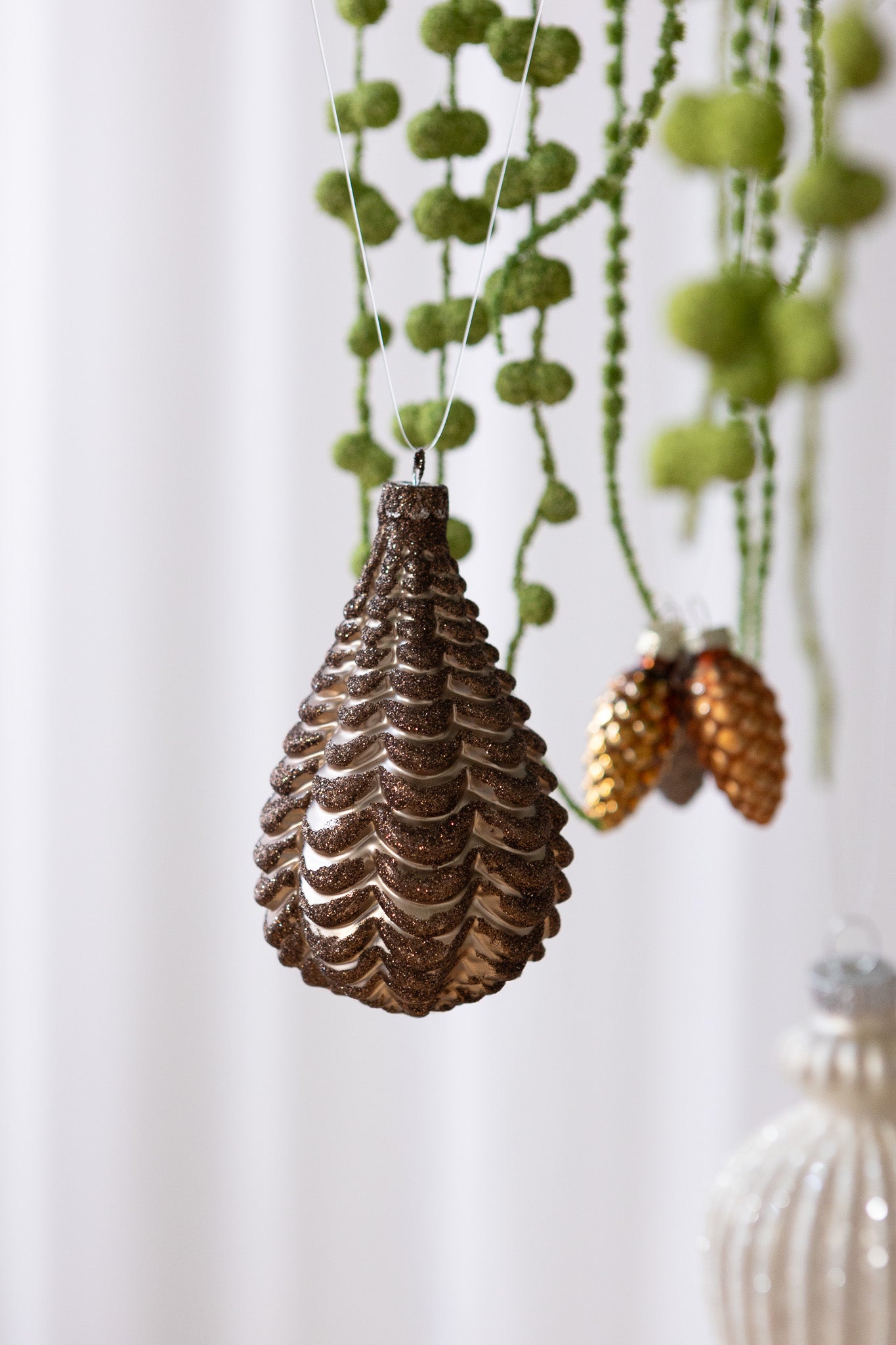 Nærbillede af Dråbeformet julekugle med koglemønster i brun med glitter