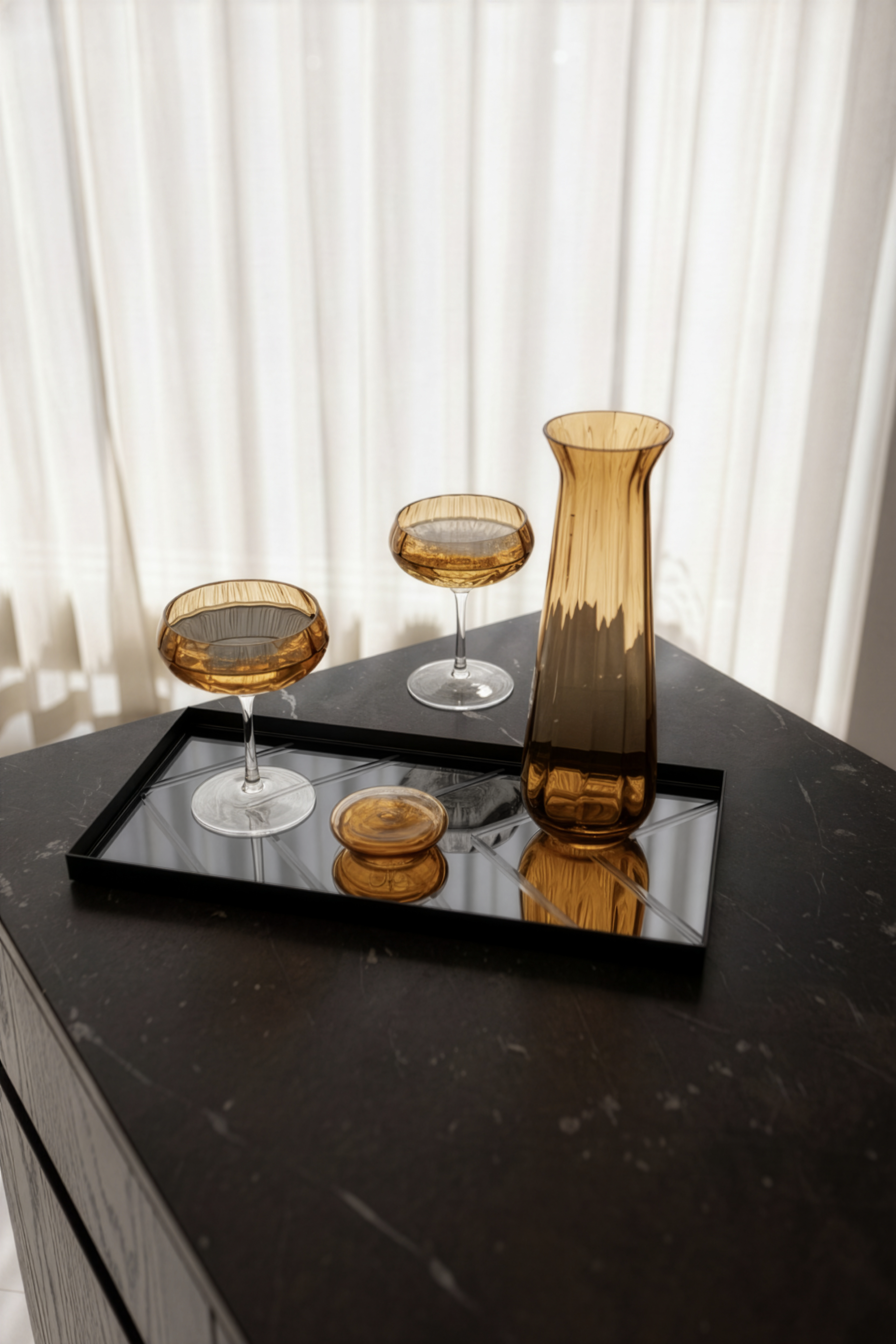 Grå spejlbakke med herringbone mønster stylet med amber farvede cocktailglas og karaffel på en køkkenø.