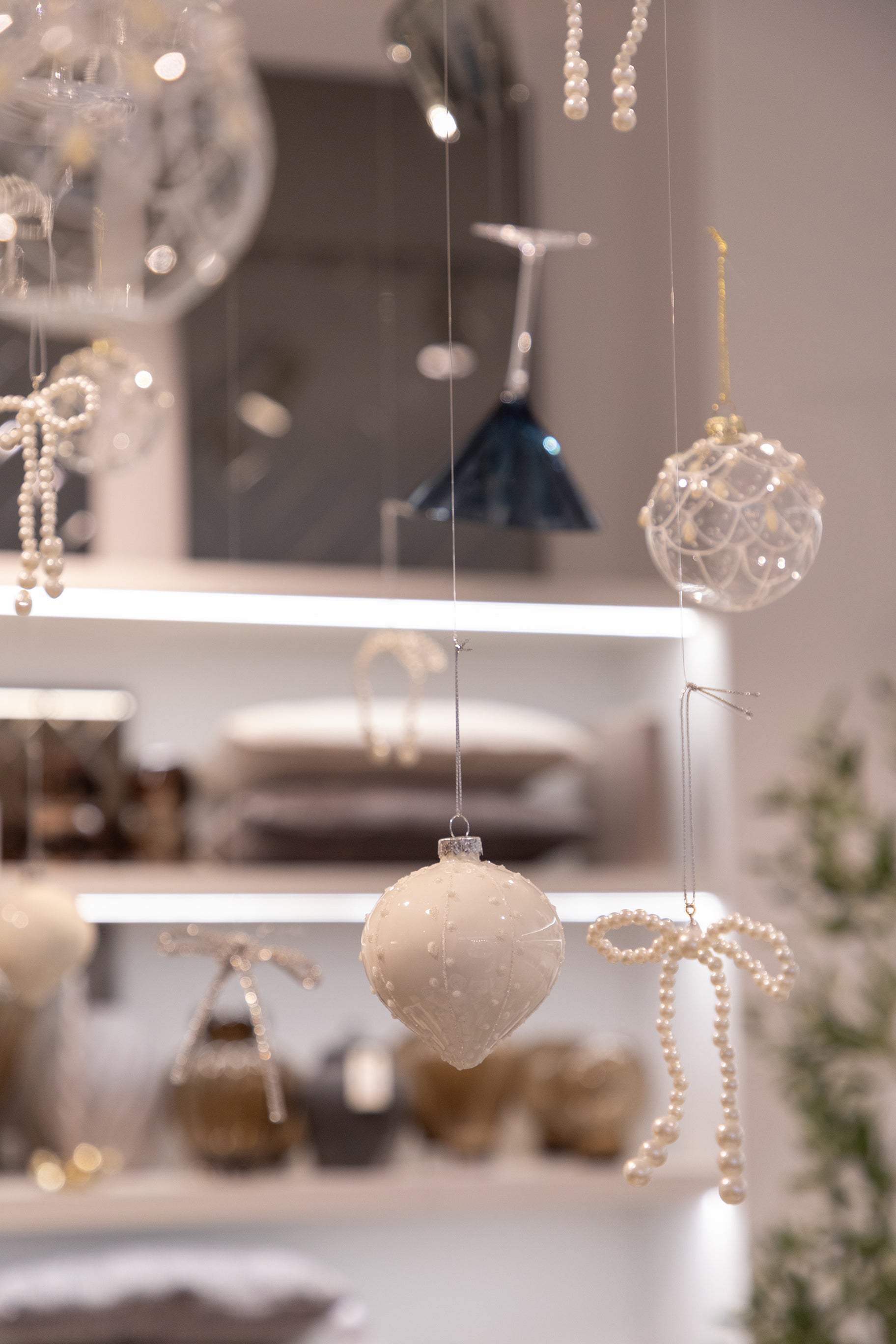 Billede af hvid julekugle med fine detaljer, der hænger fra loftet blandt andre julekugler og glas.