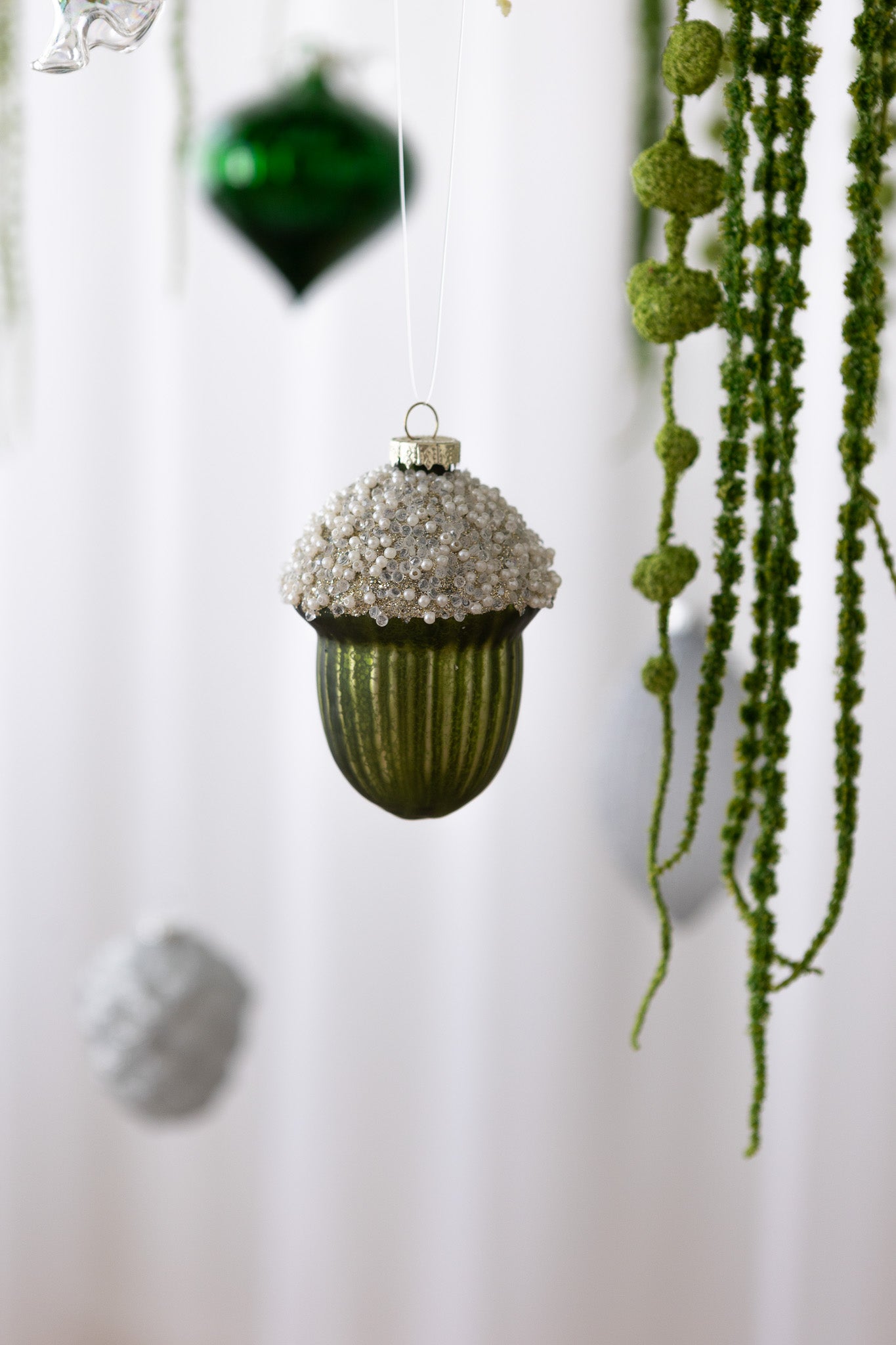 Nærbillede af Agern-formet julekugle i grøn med hvide og klare perler samt guldglimmer i toppen