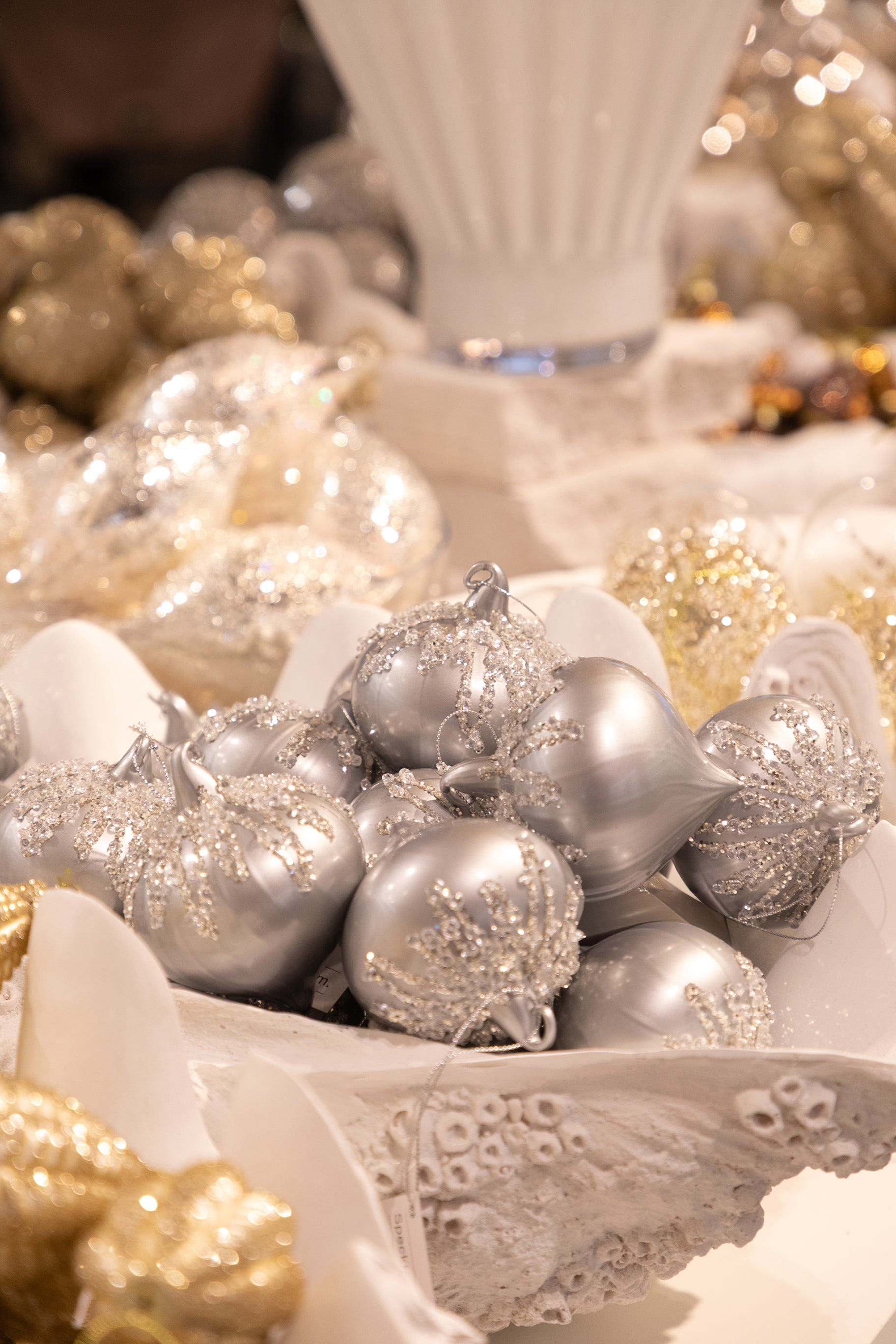 Sølv julekugle med krystal detaljer, der ligger blandt flere julekugler i en hvid muslinge skål.