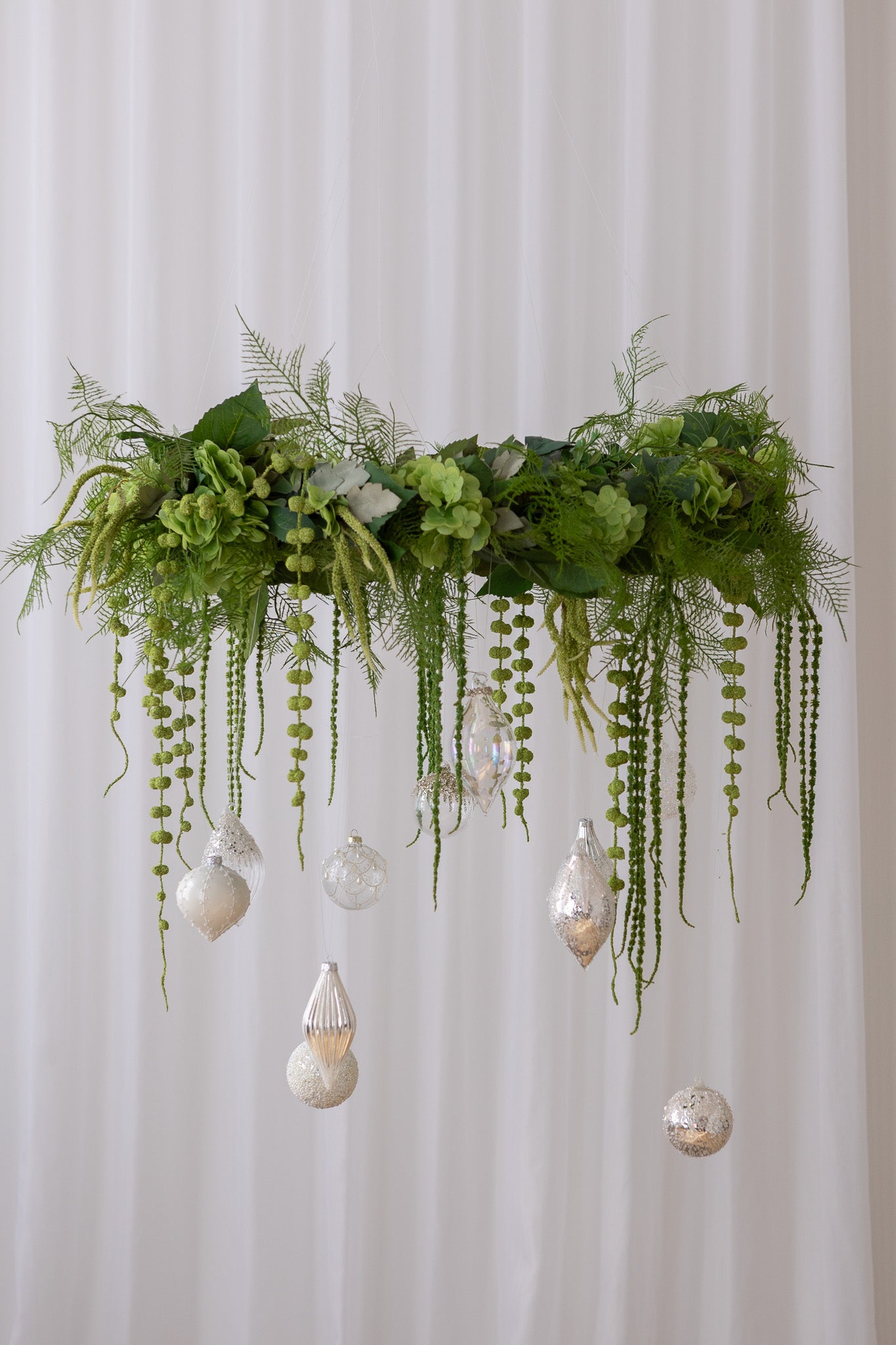 Billede af en krans, hvor der hænger julekugler i hvide og sølv nuancer fra.