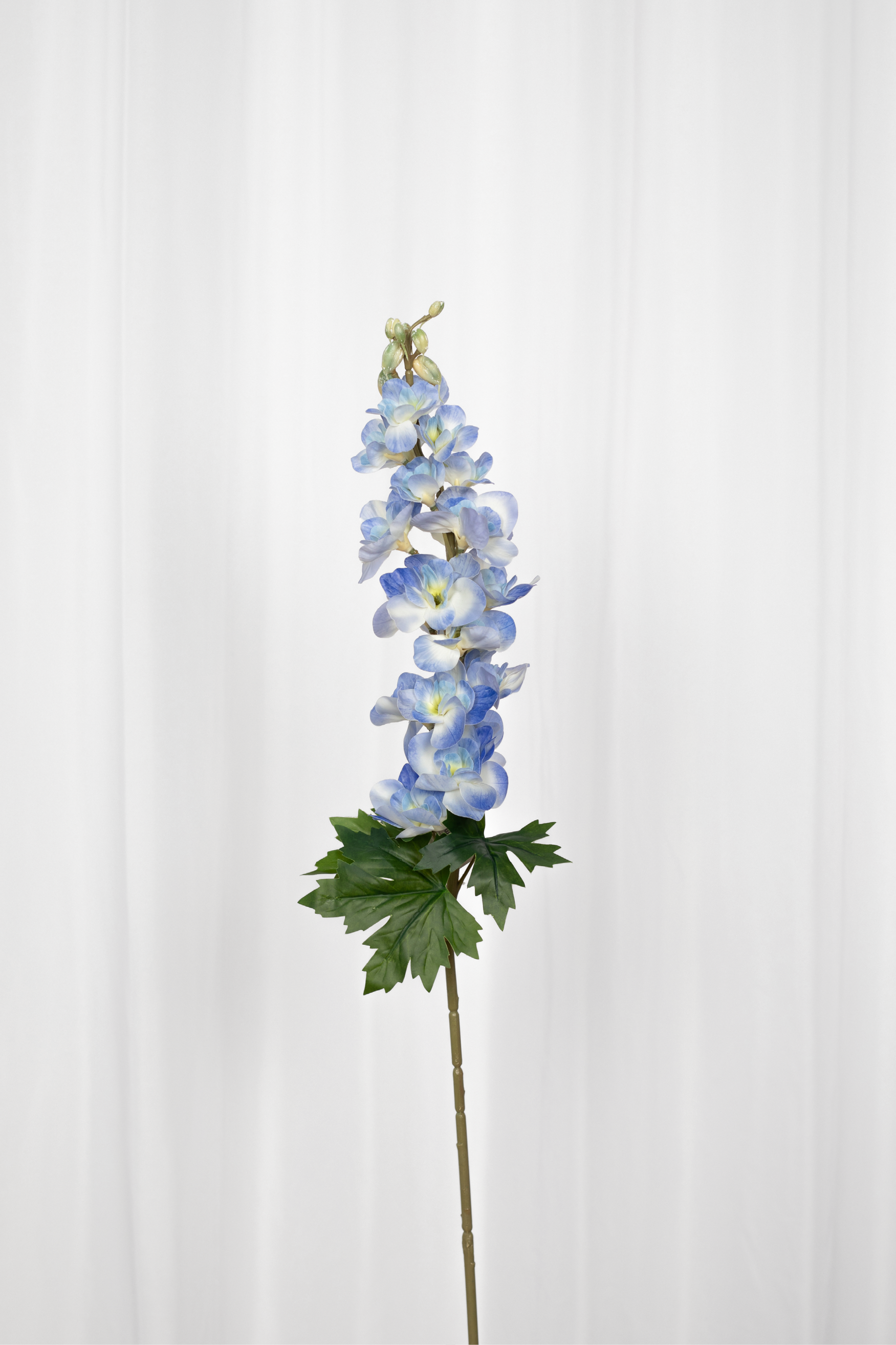 Kunstig consolida blomst i blå med grønne blade i bunden.