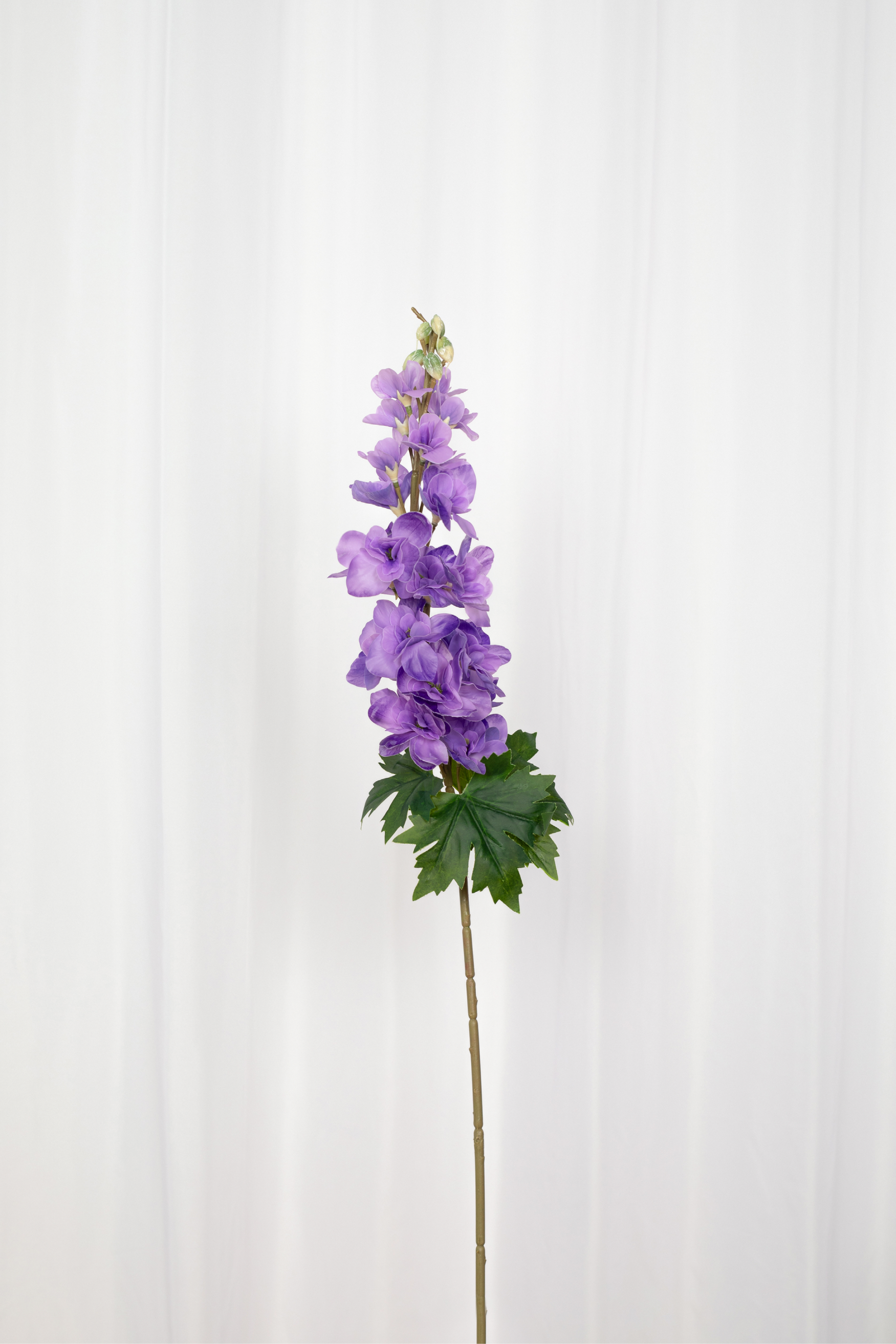 Kunstig consolida i lilla med grønne blade i bunden.