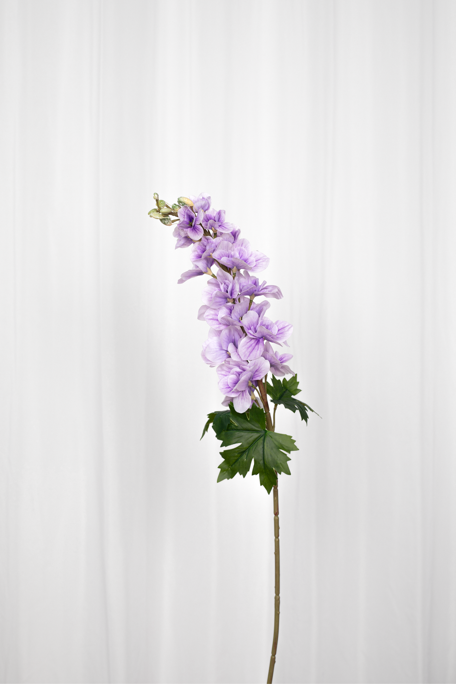 Kunstig consolida blomst i en lyselilla farve med grønne blade i bunden.