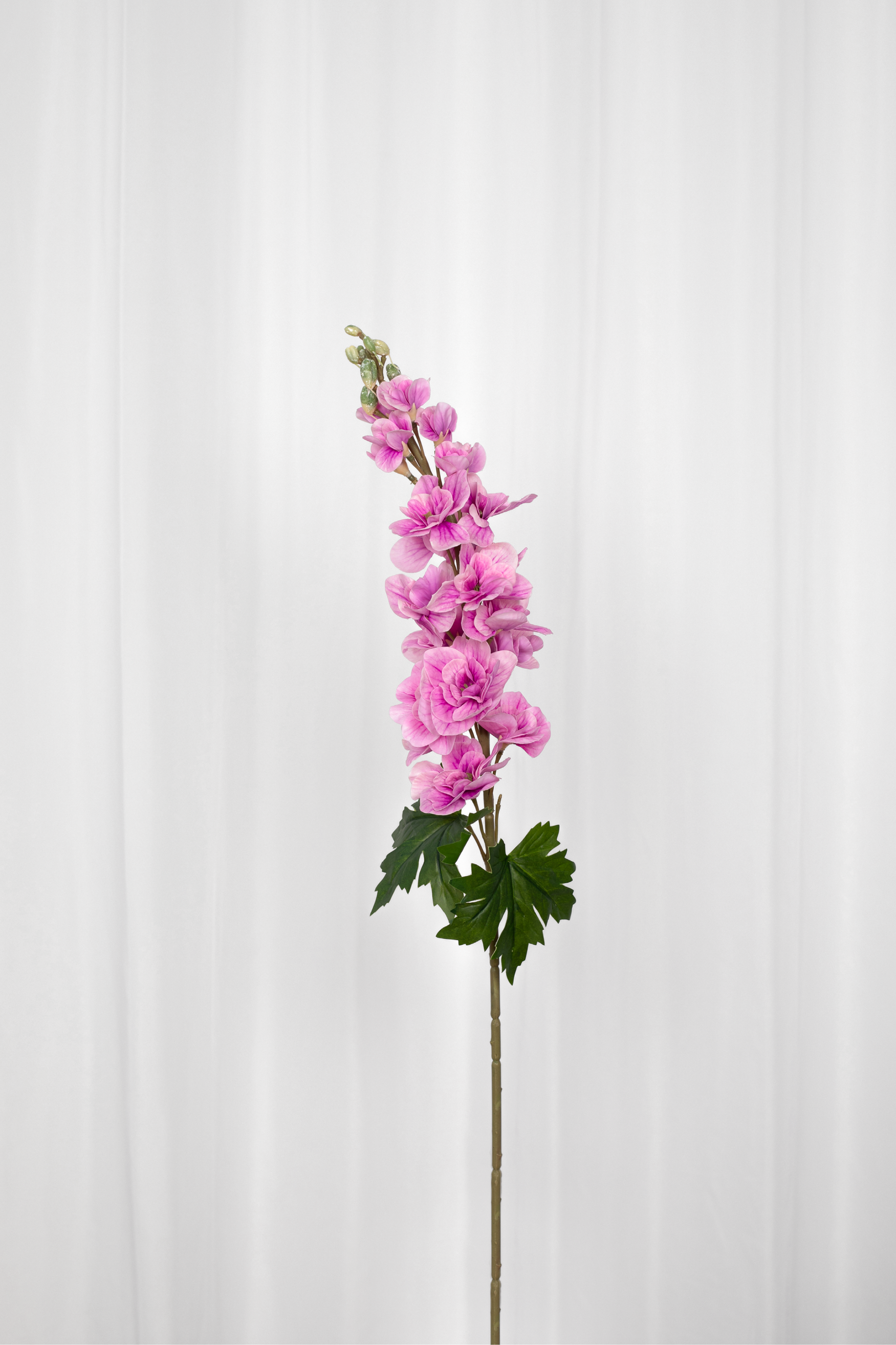 Kunstig consolida blomst i pink med grønne blade i bunden.