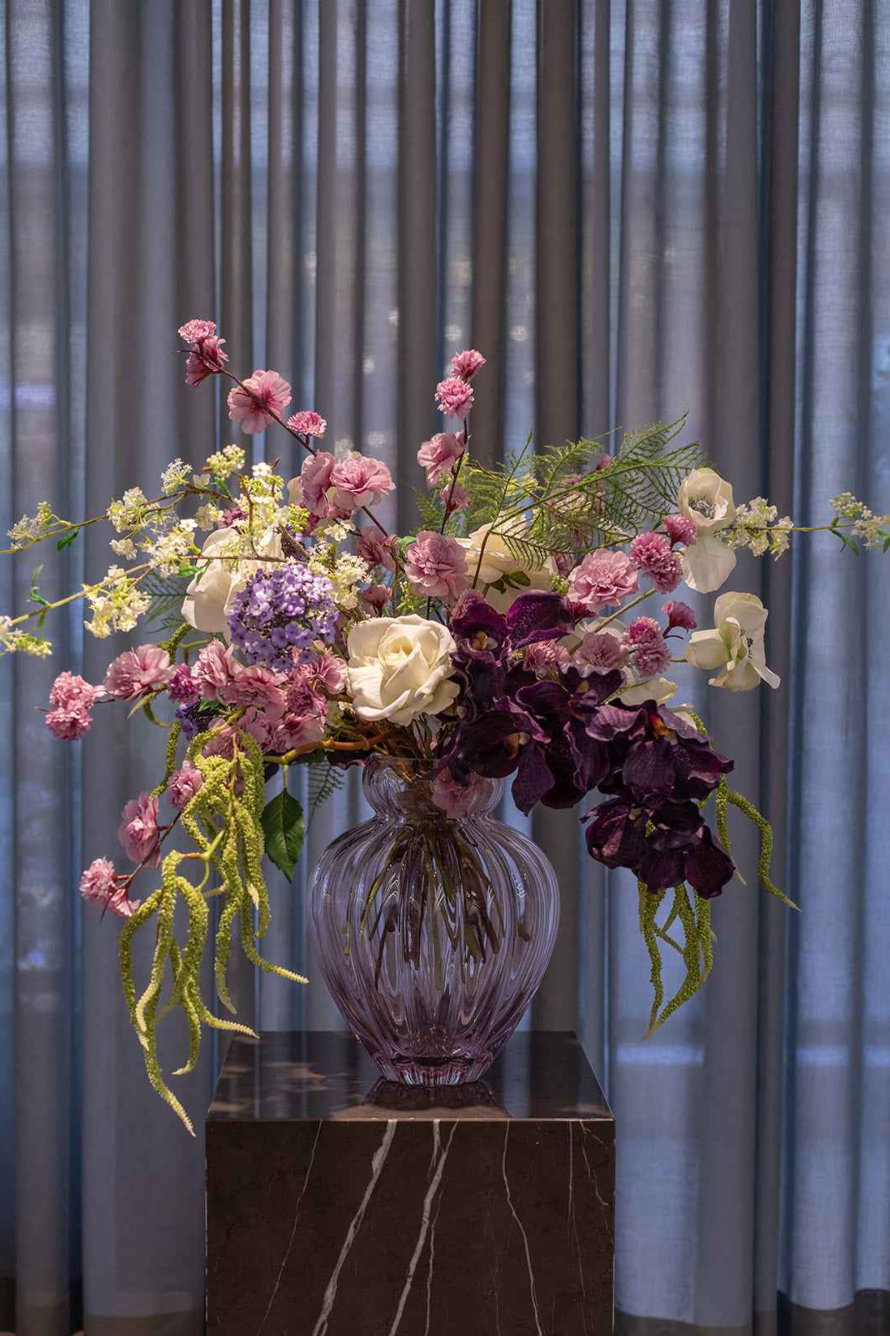 Kunstig buket i lilla og lyserøde nuancer i en lyserød glasvase.