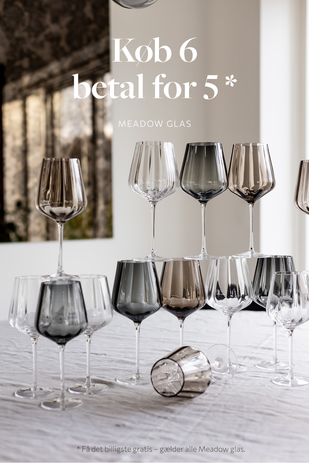 Reklamebillede med teksten "Køb 6 betal for 5 – Meadow glas". På et dækket bord står en samling Meadow glas i klare, røgfarvede og brune nuancer arrangeret i små grupper og stablet dekorativt. Et enkelt glas ligger på siden foran. Nederst står teksten: "Få det billigste gratis – gælder alle Meadow glas".