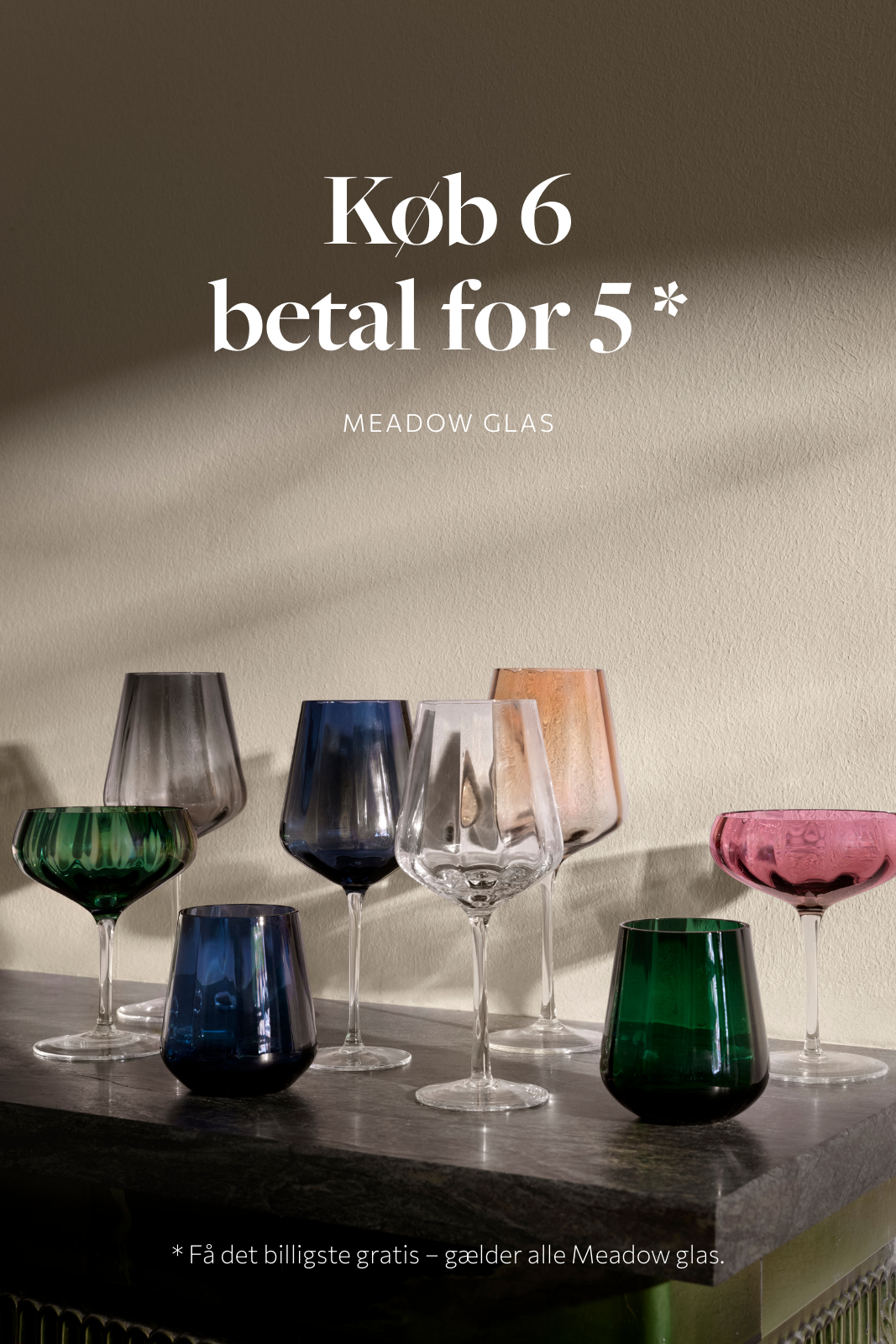 Reklamebillede med teksten "Køb 6 betal for 5 – Meadow glas". Foran en lys beige væg står et udvalg af Meadow glas i forskellige farver og former, herunder grønne, blå, rosa, klare og røgfarvede glas. Nederst står der: "Få det billigste gratis – gælder alle Meadow glas".