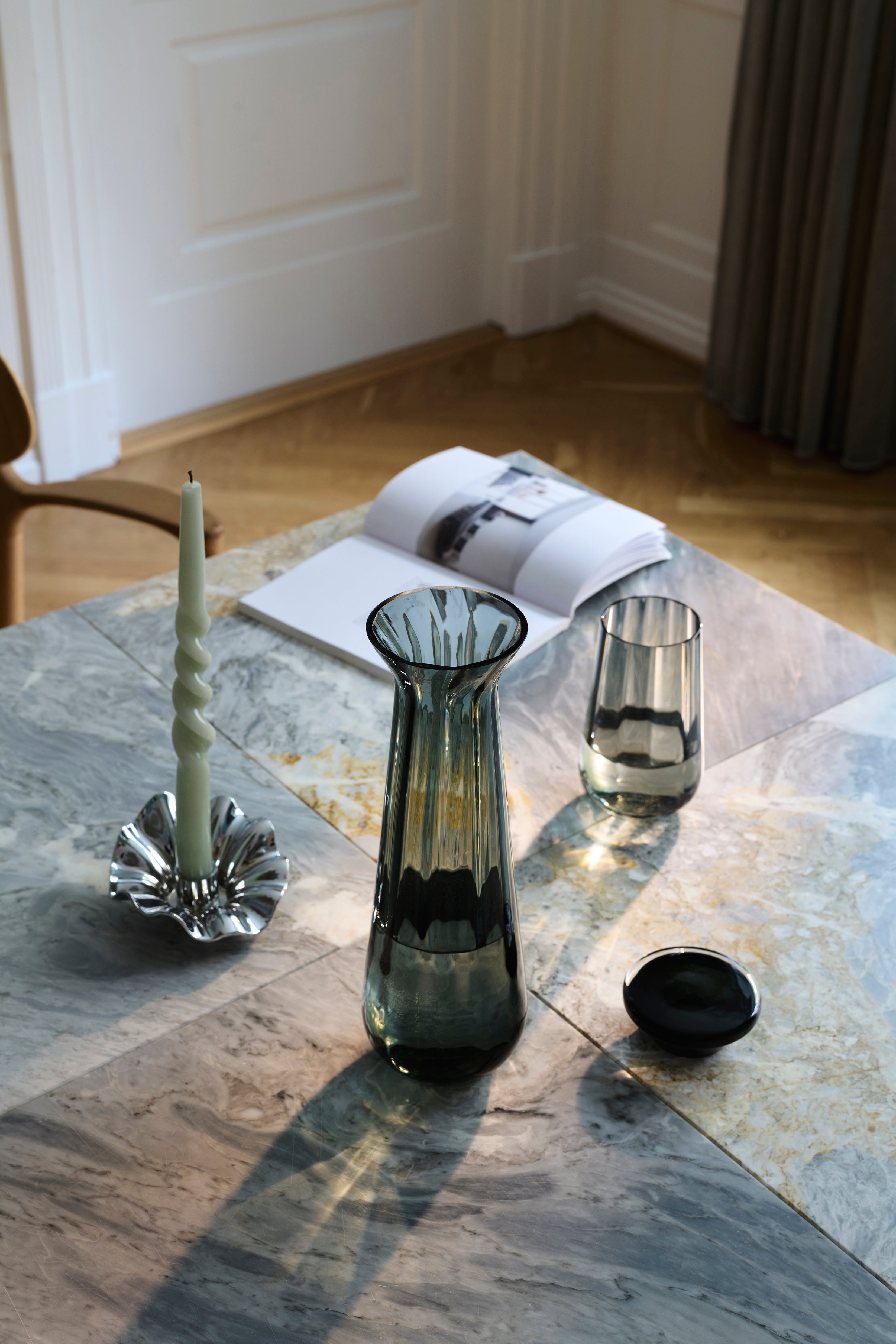 Højt drikkeglas i Meadow serien i grå med stribet mønster. Glasset er stylet på et spisebord sammen med Meadow karaflen og Lea lysestagen.