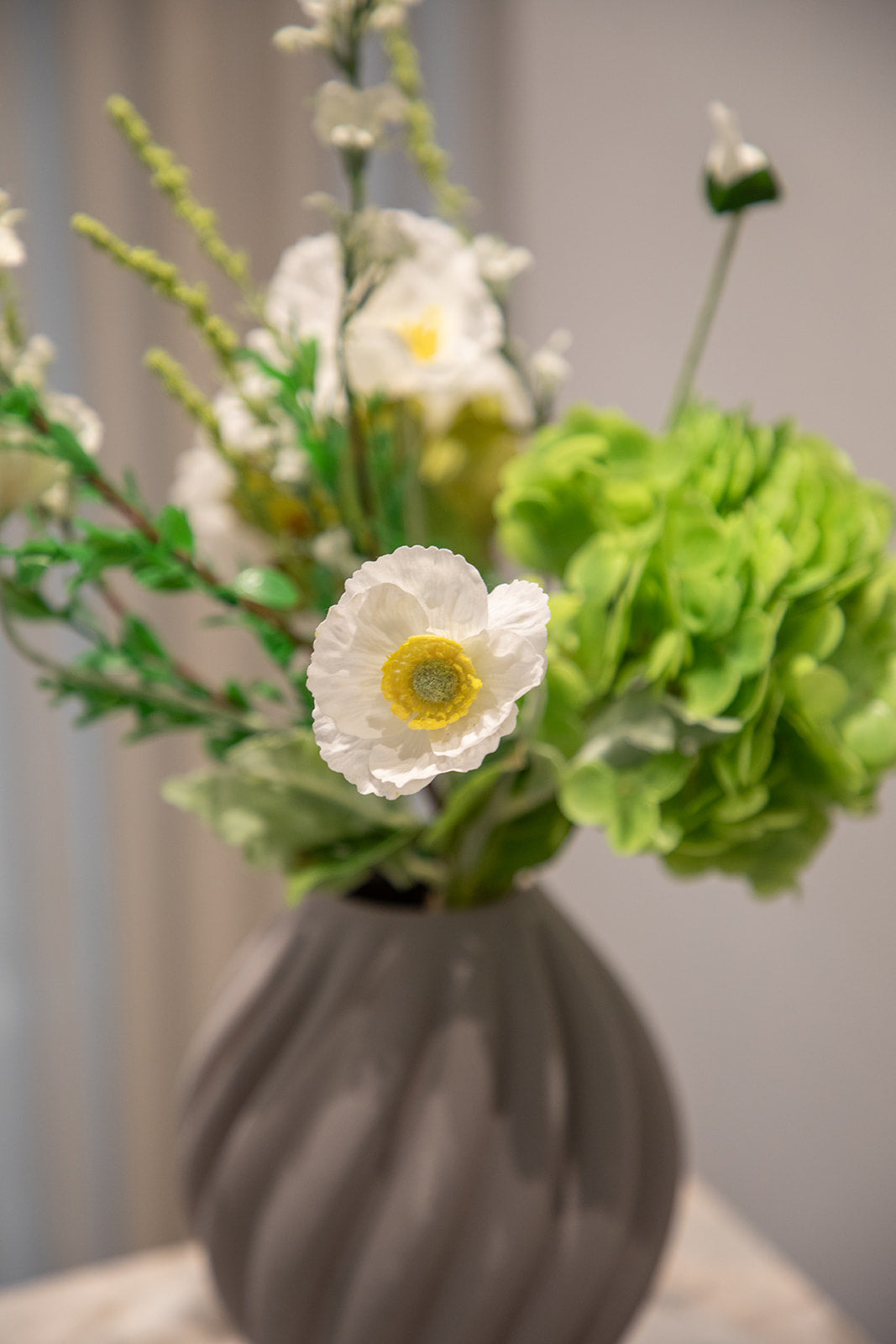 Nærbillede af buket af kunstige blomster i hvide og grønne nuancer. Placeret i en grå keramikvase.