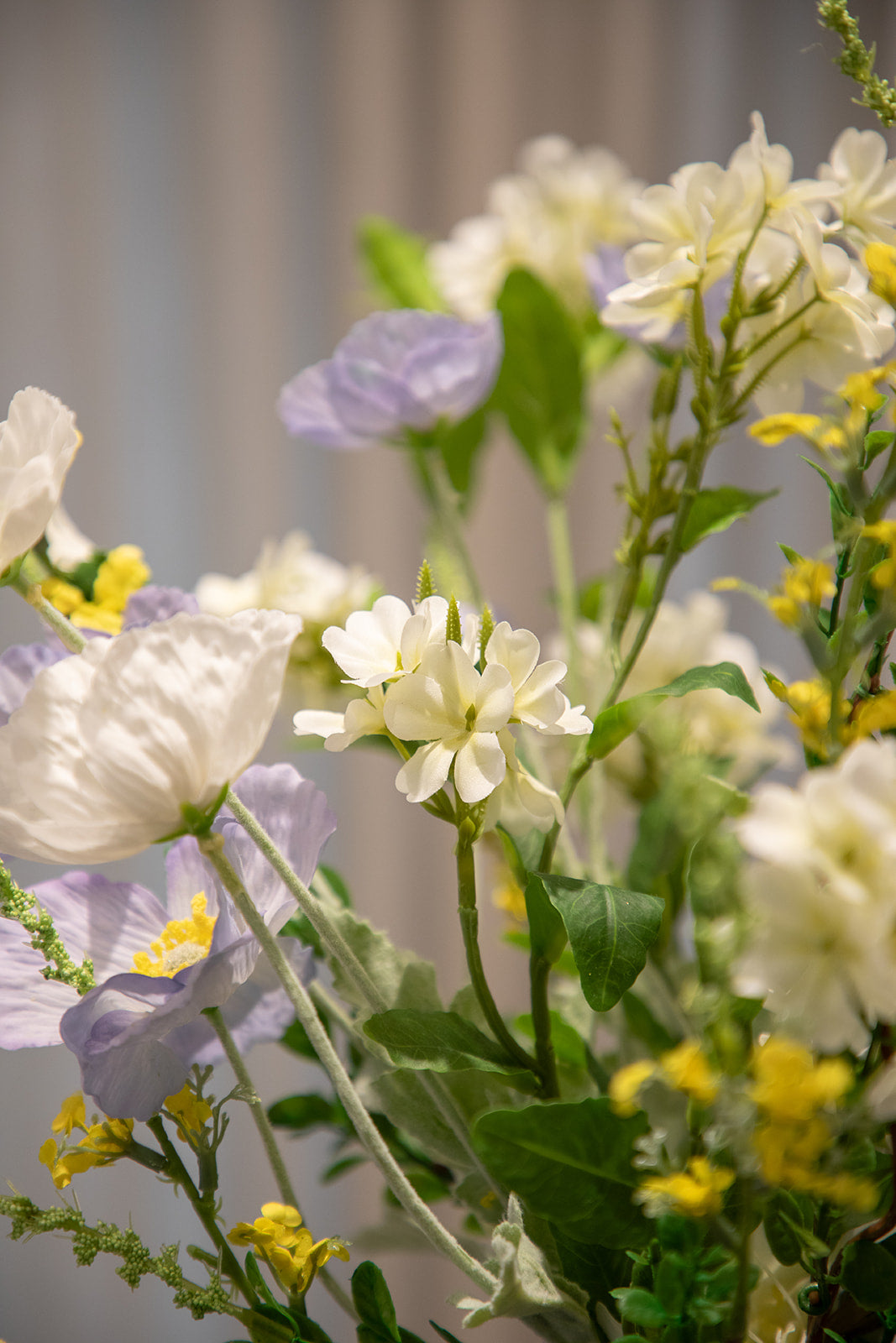 Nærbillede af en buket af kunstige blomster i lilla, hvide, gule og grønne nuancer.
