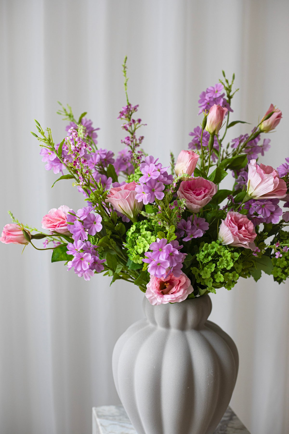 Nærbillede af markbuket af kunstige, naturtro blomster i lilla og lyserøde nuancer.