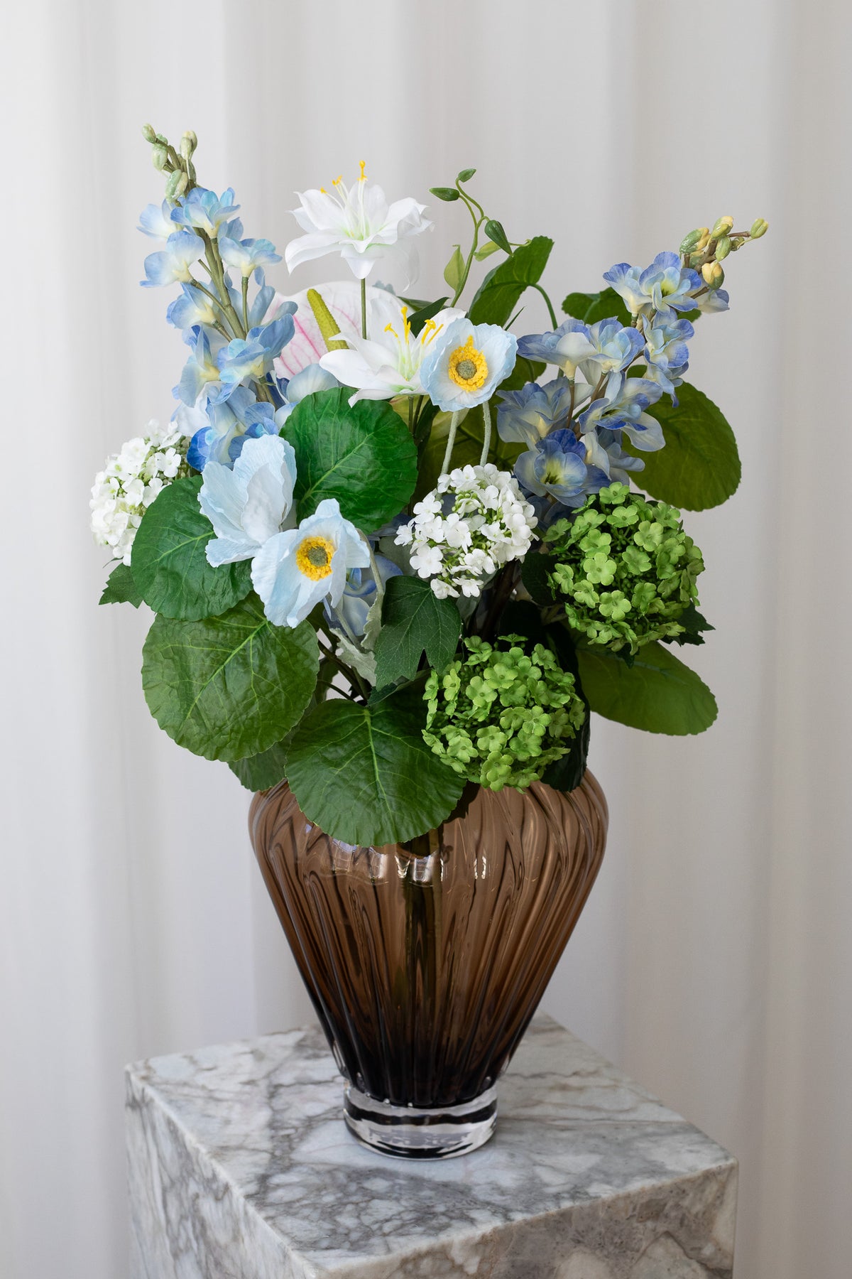 Blå kunstig buket med grønne blade og hvide blomsterstilke. Buketten ser utroligt ægte ud.