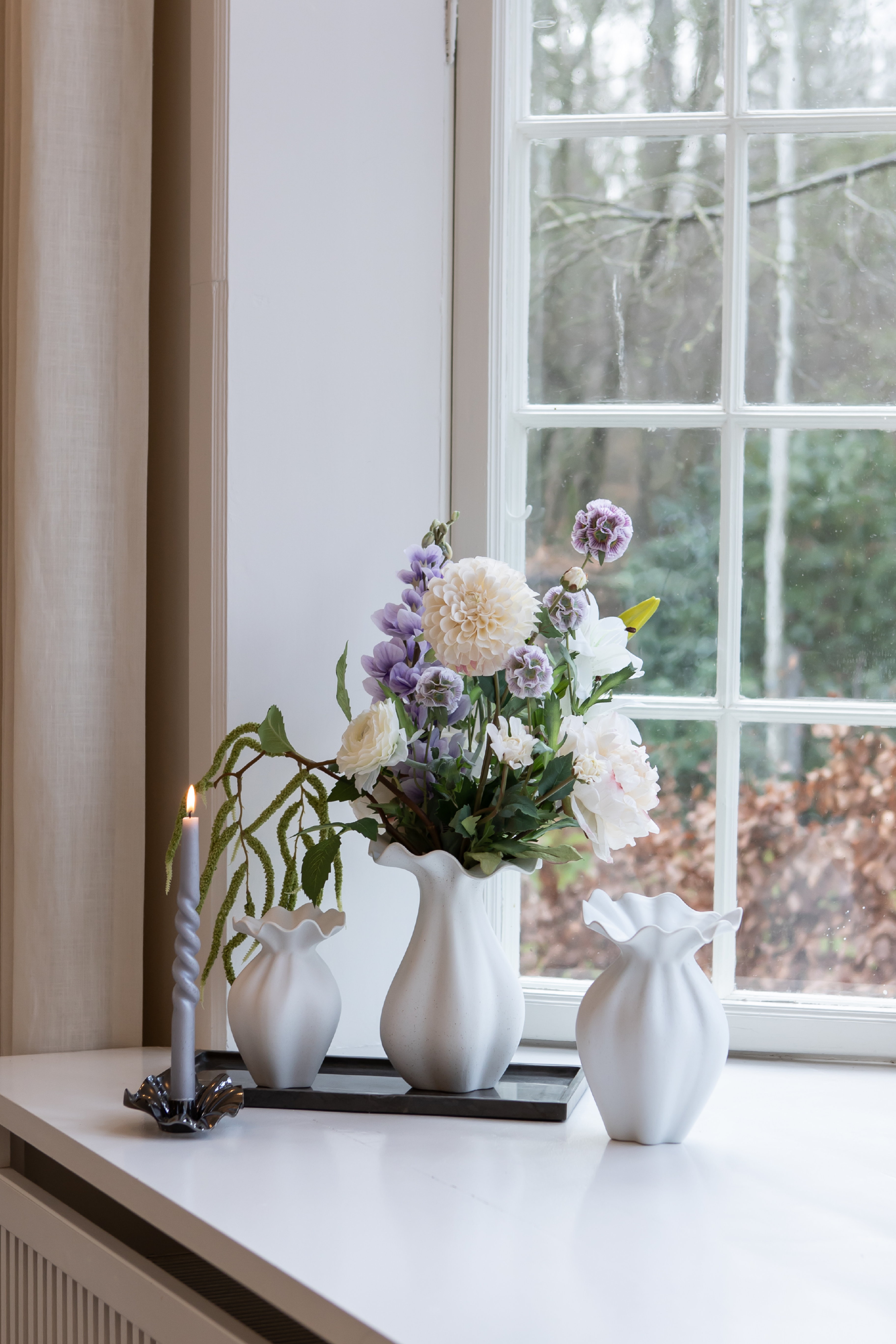 Nellie vaser I off white stylet på en marmorbakke og med en metal lysestage med samme organiske former.