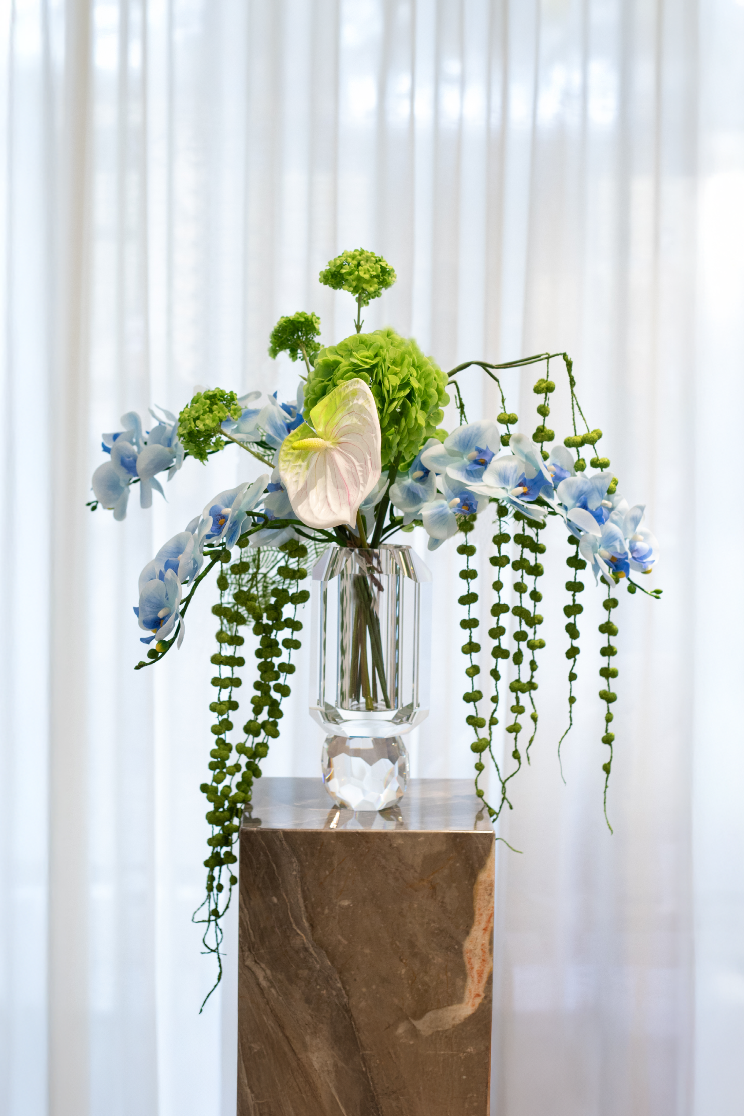 Kunstige blomster.
Buketten er stylet i Storm krystal vasen.
Buketten indeholder
3 x blue orchid (9 heads)
2 x green hanging branch no. 3
1 x Green hydrangea
1 x Green Hydrangea branch
1 x green fern branch