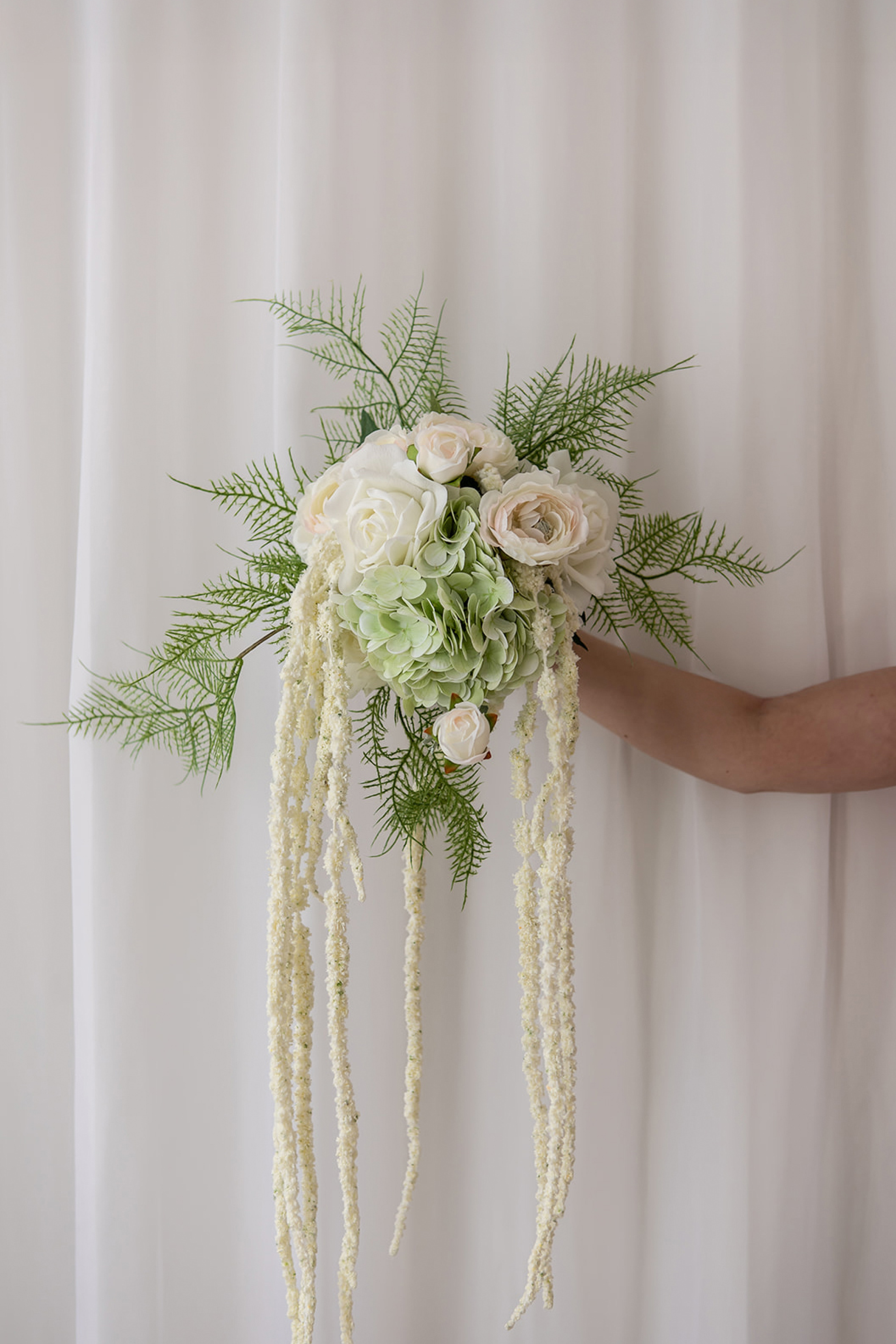 Brudebuket sammensat af kunstige blomster i farvenuancerne grøn og hvid.