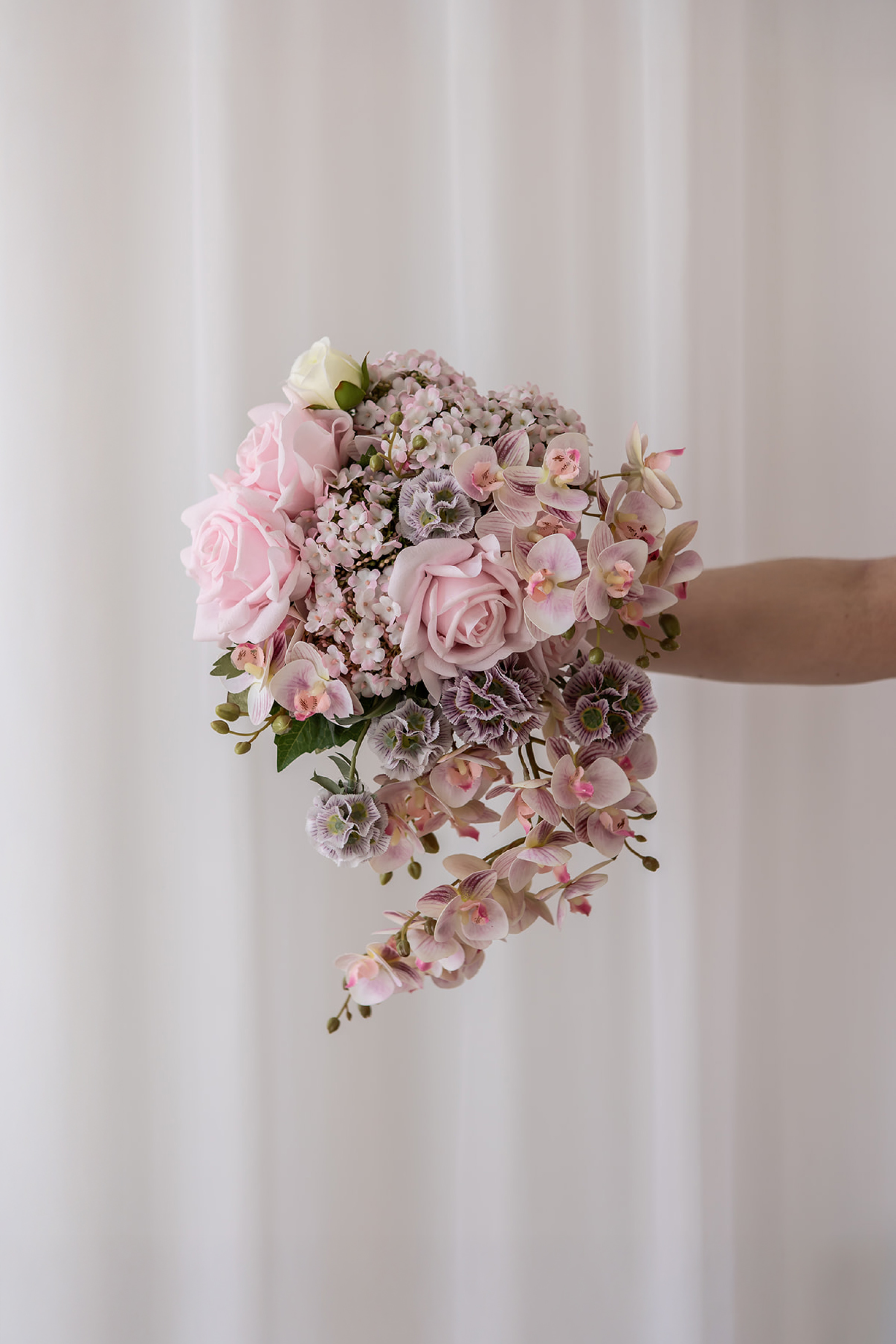 Brudebuket sammensat af kunstige blomster i farvenuancen lyserød.