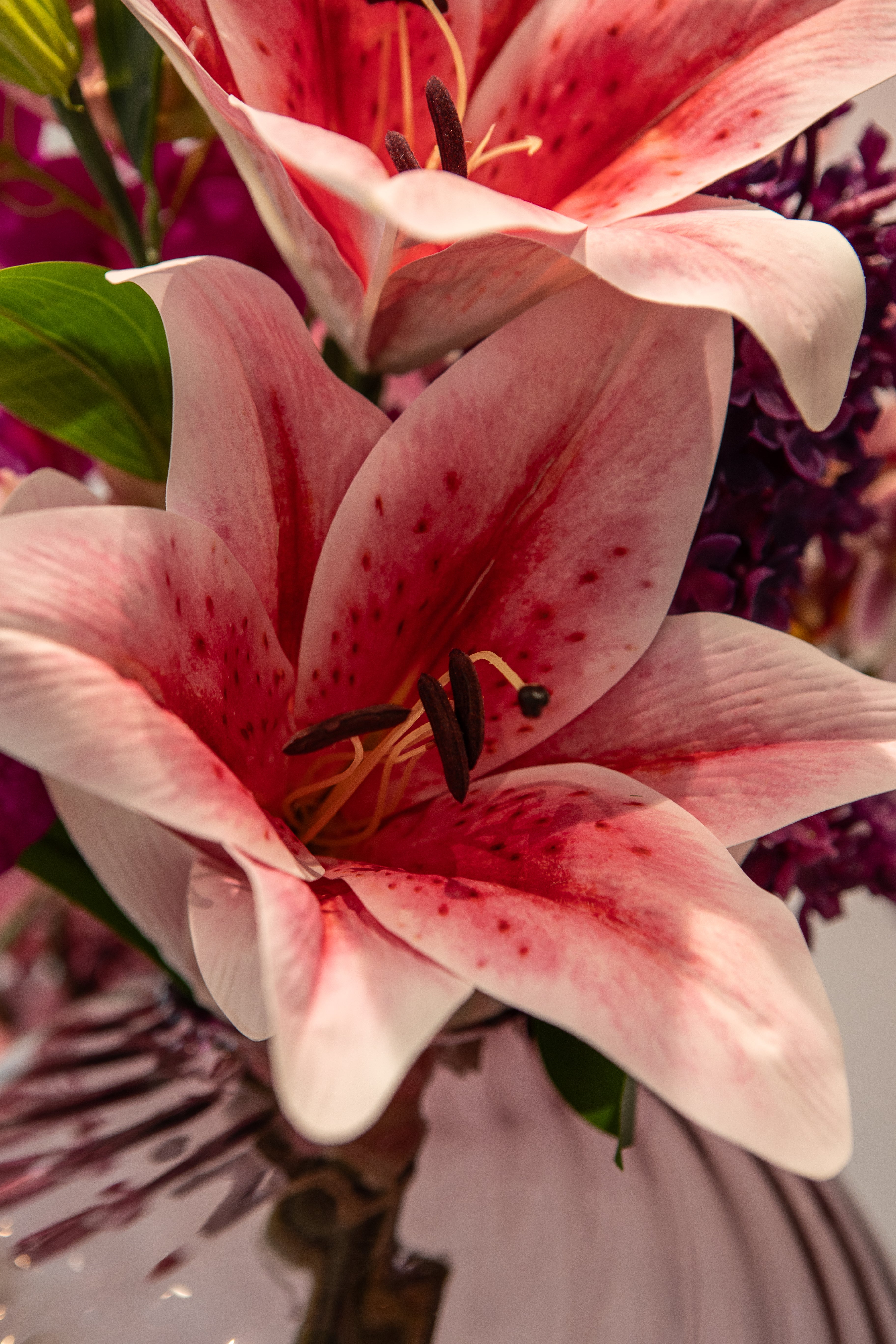 Nærbillede af en stor lyserød lilje i en farverig buket i lyserøde og lille nuancer, i en plumfarvet glasvase.