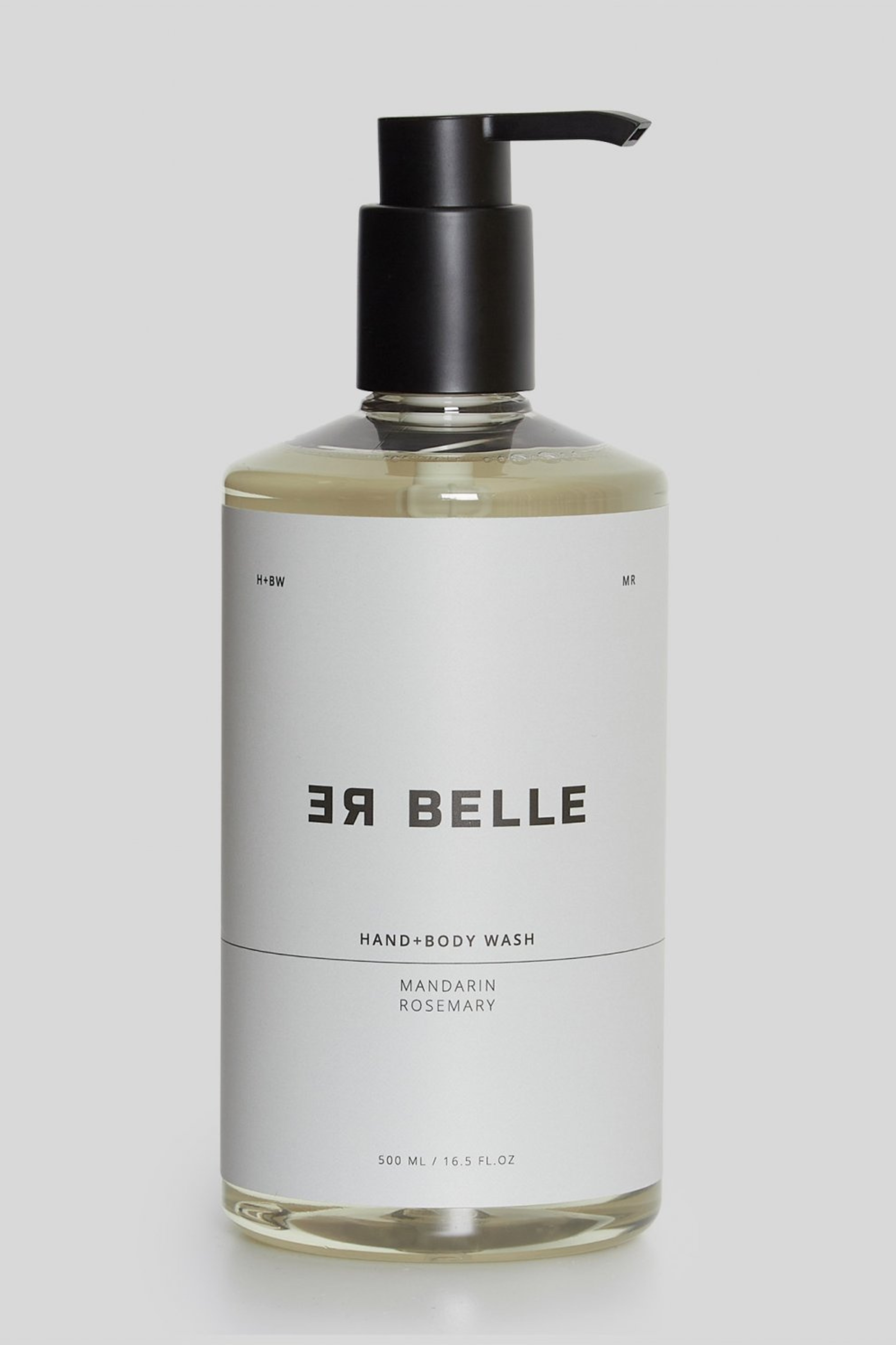 En gennemsigtig plastflaske med sort pumpe indeholdende en lys væske. Etiketten er hvid med sort tekst: “RE BELLE HAND+BODY WASH, MANDARIN ROSEMARY, 500 ML