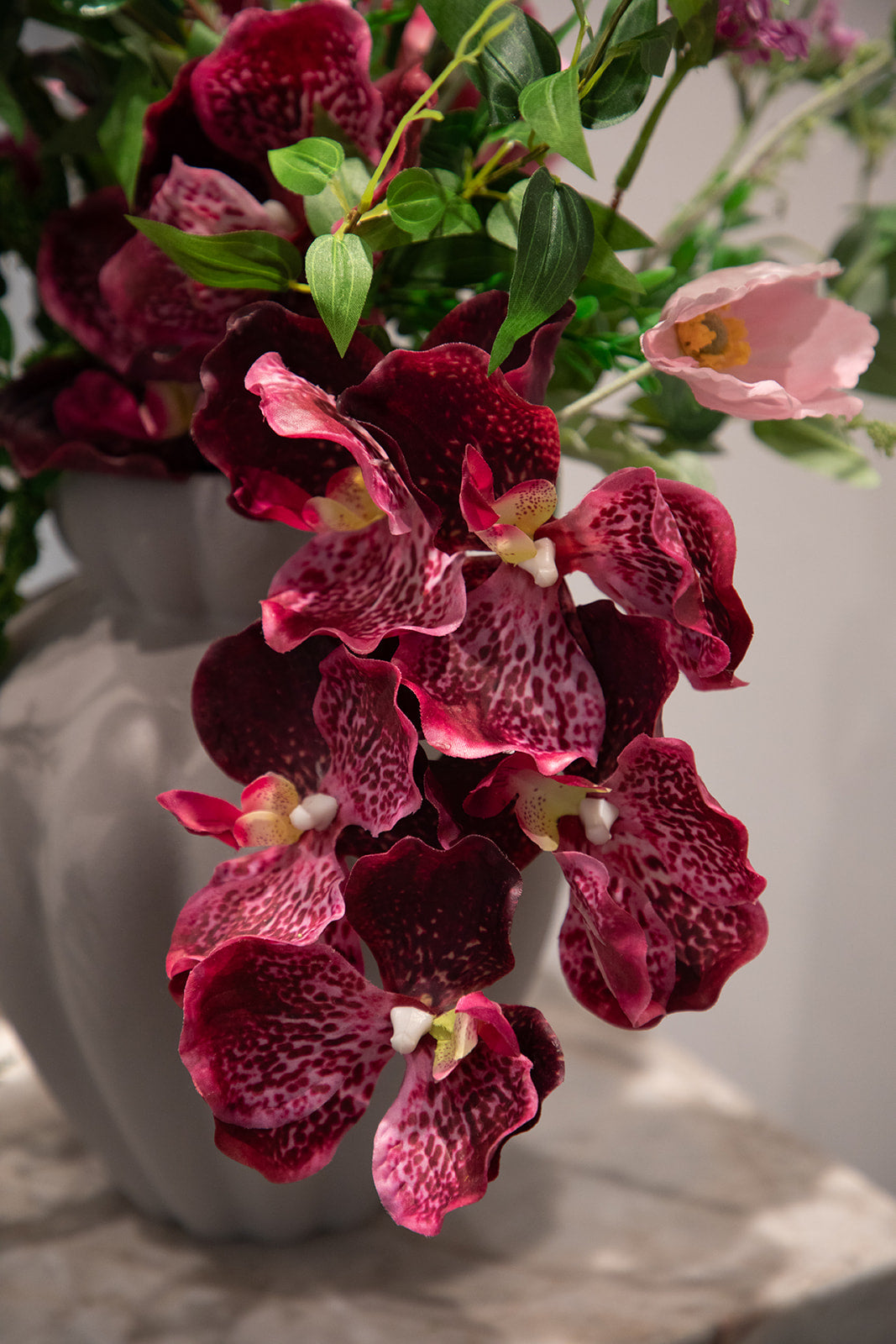 Nærbillede af en buket af kunstige blomster i rosa nuancer. Placeret i en keramikvase, der står på en marmor pedestal.